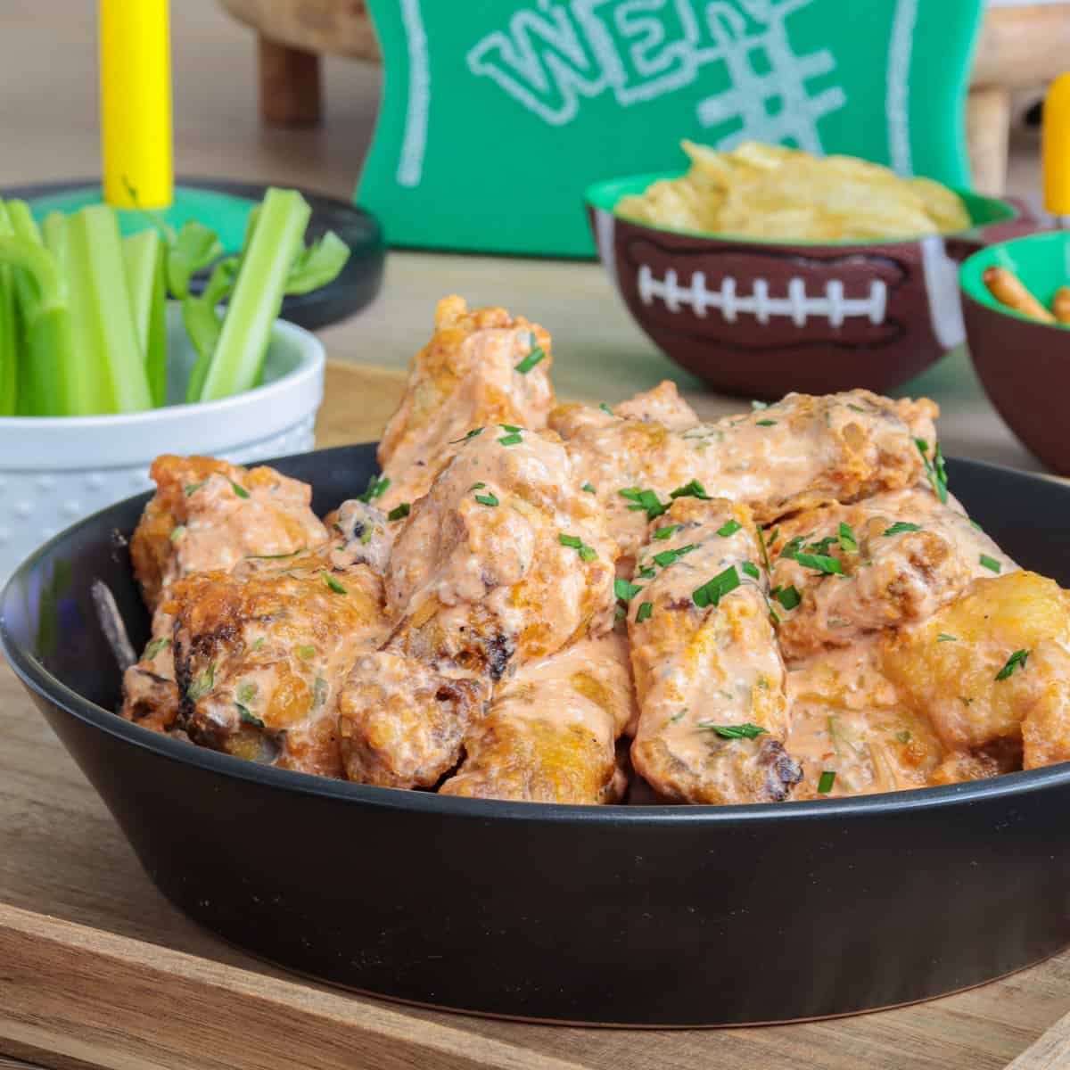 Buffalo ranch chicken wings in a bowl with football decor on table.