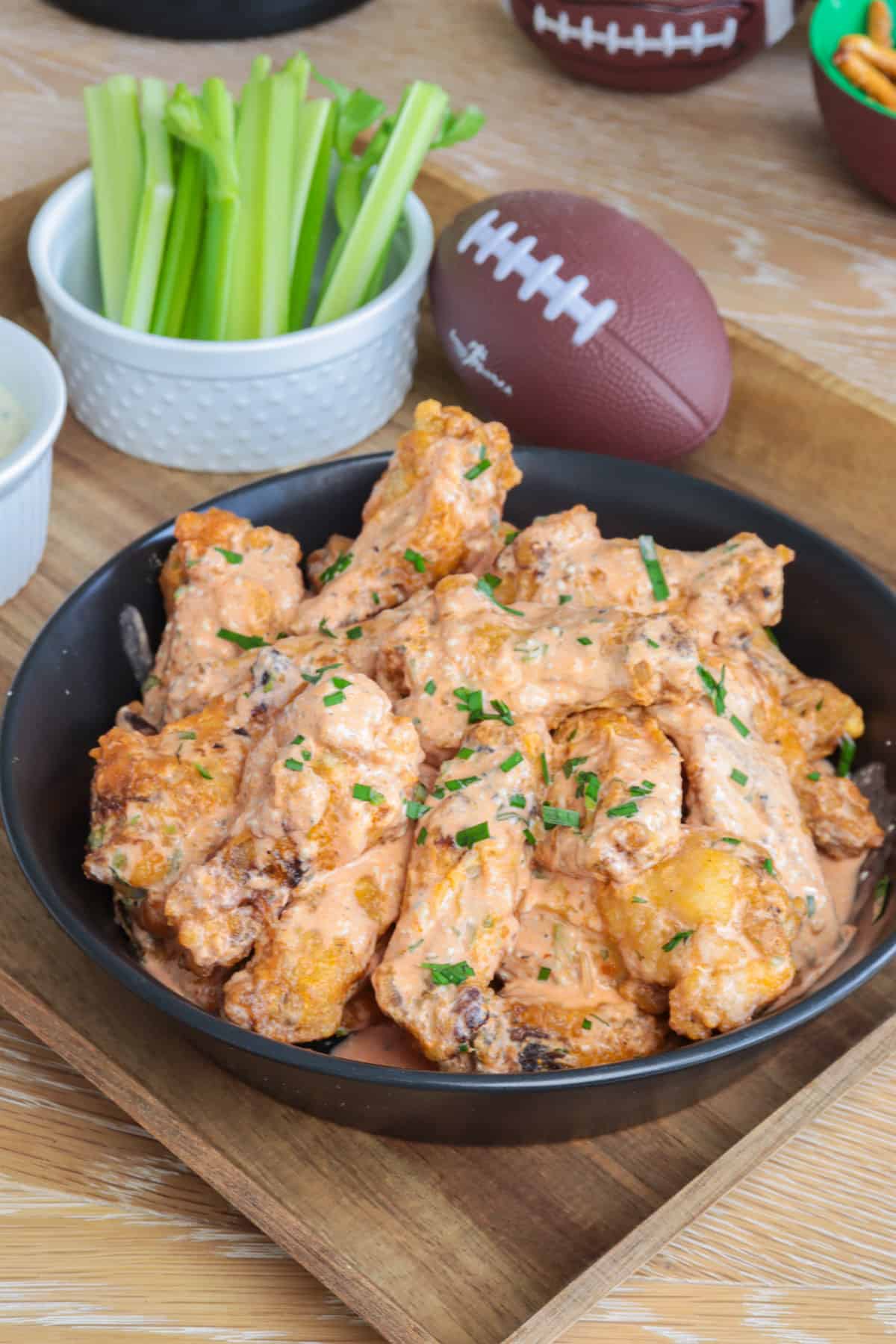 Crispy chicken wings with buffalo ranch sauce in a bowl with football and celery sticks.