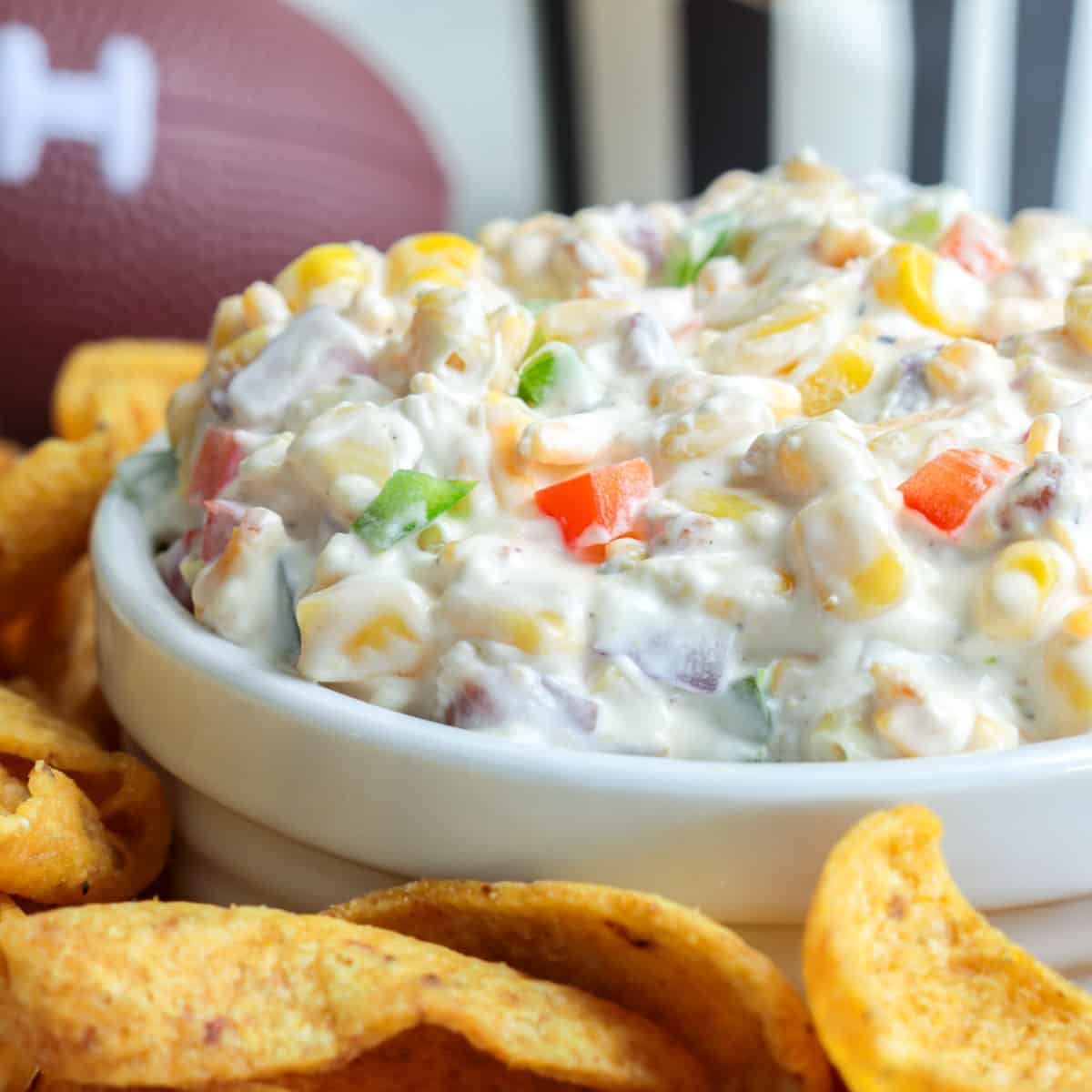 Cold corn dip in a white bowl surrounded frito scoops.