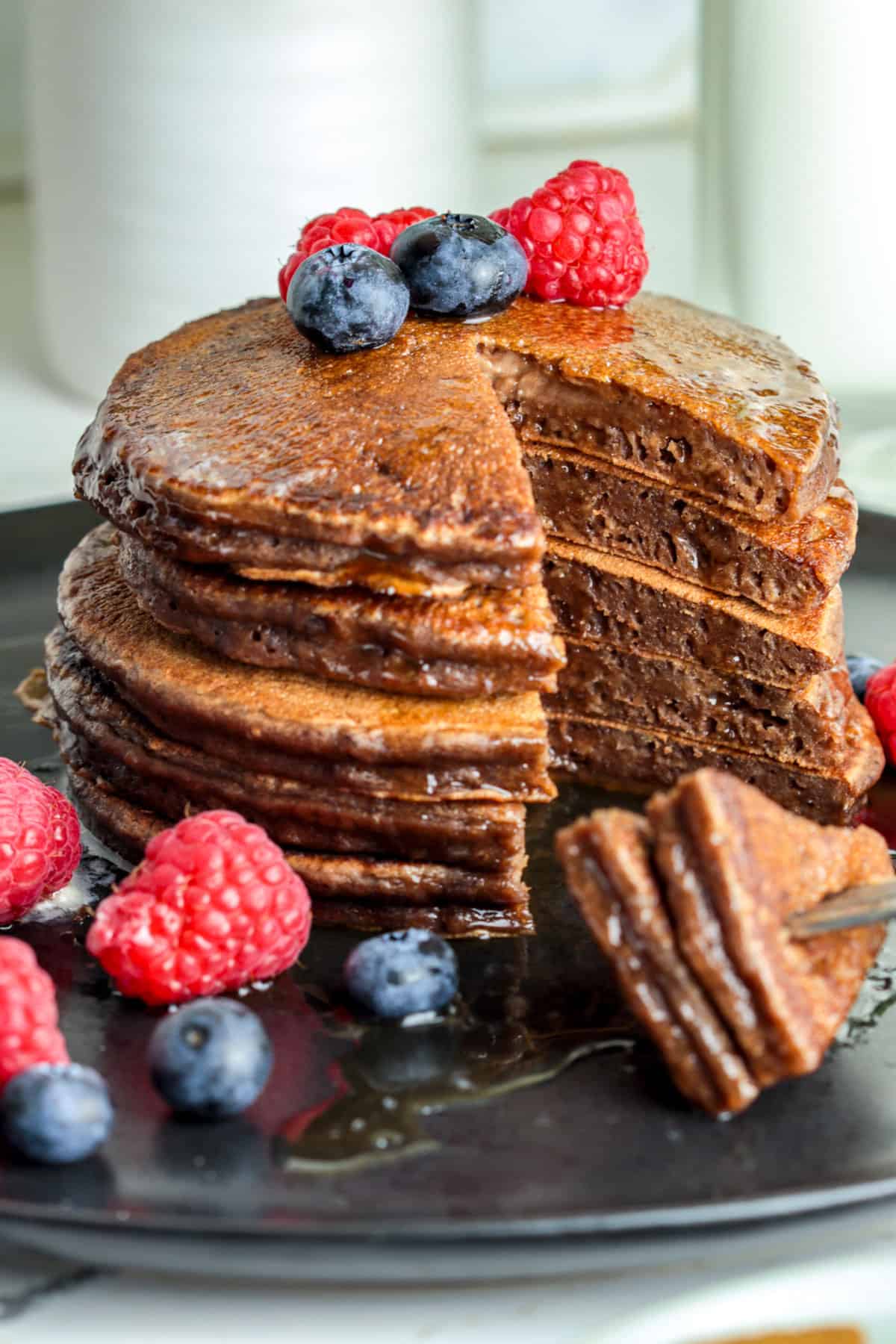 Chocolate pancakes in a stack with berries and maple syrup.