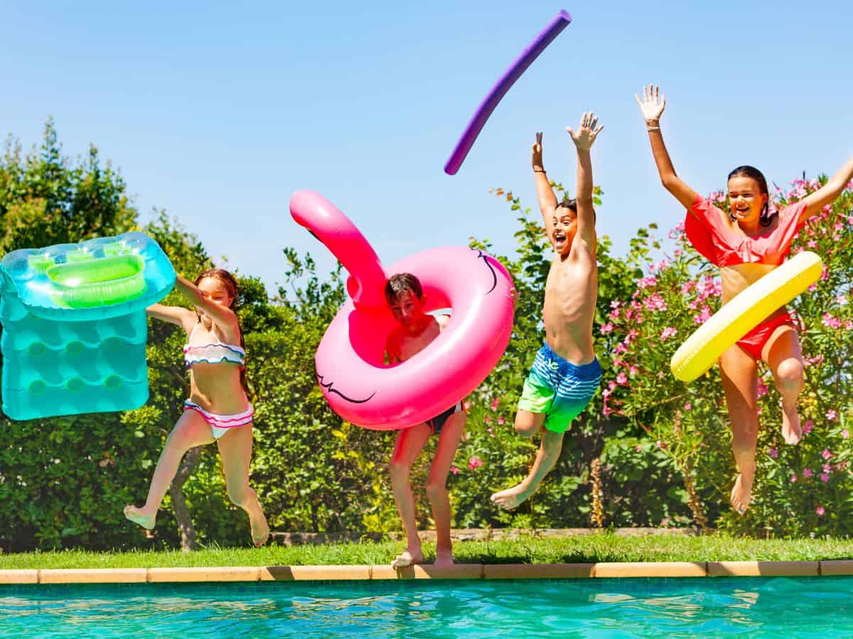 Kids jumping into a pool with floaties.