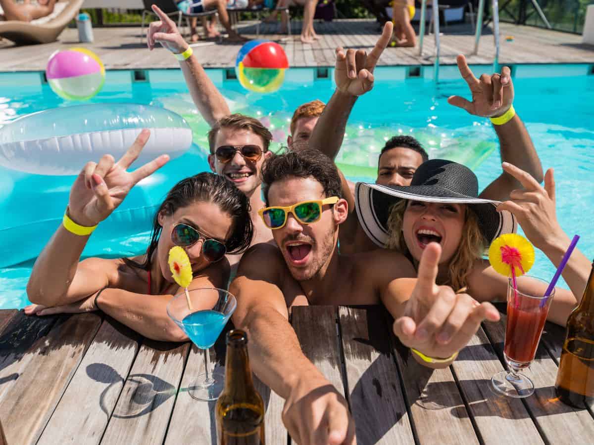 Adults at a pool party with drinks and beach balls.