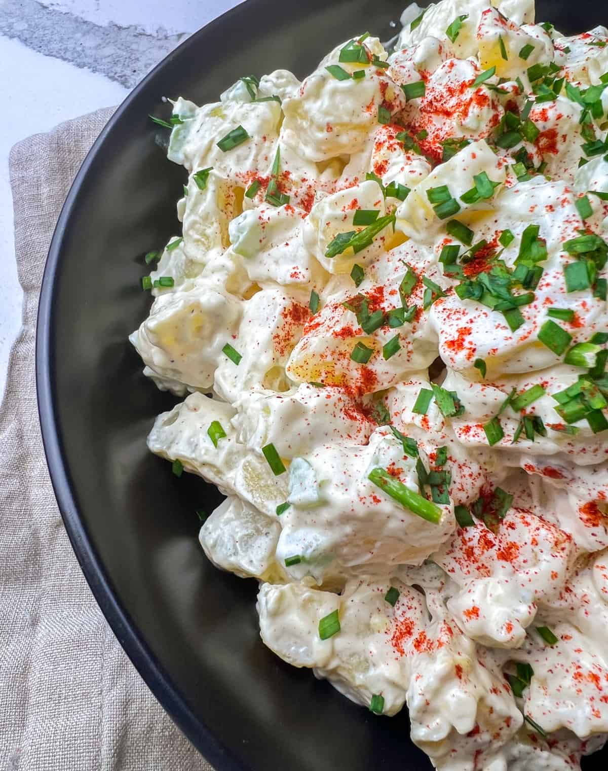 Sour cream potato salad in black dish with paprika and chives on top.