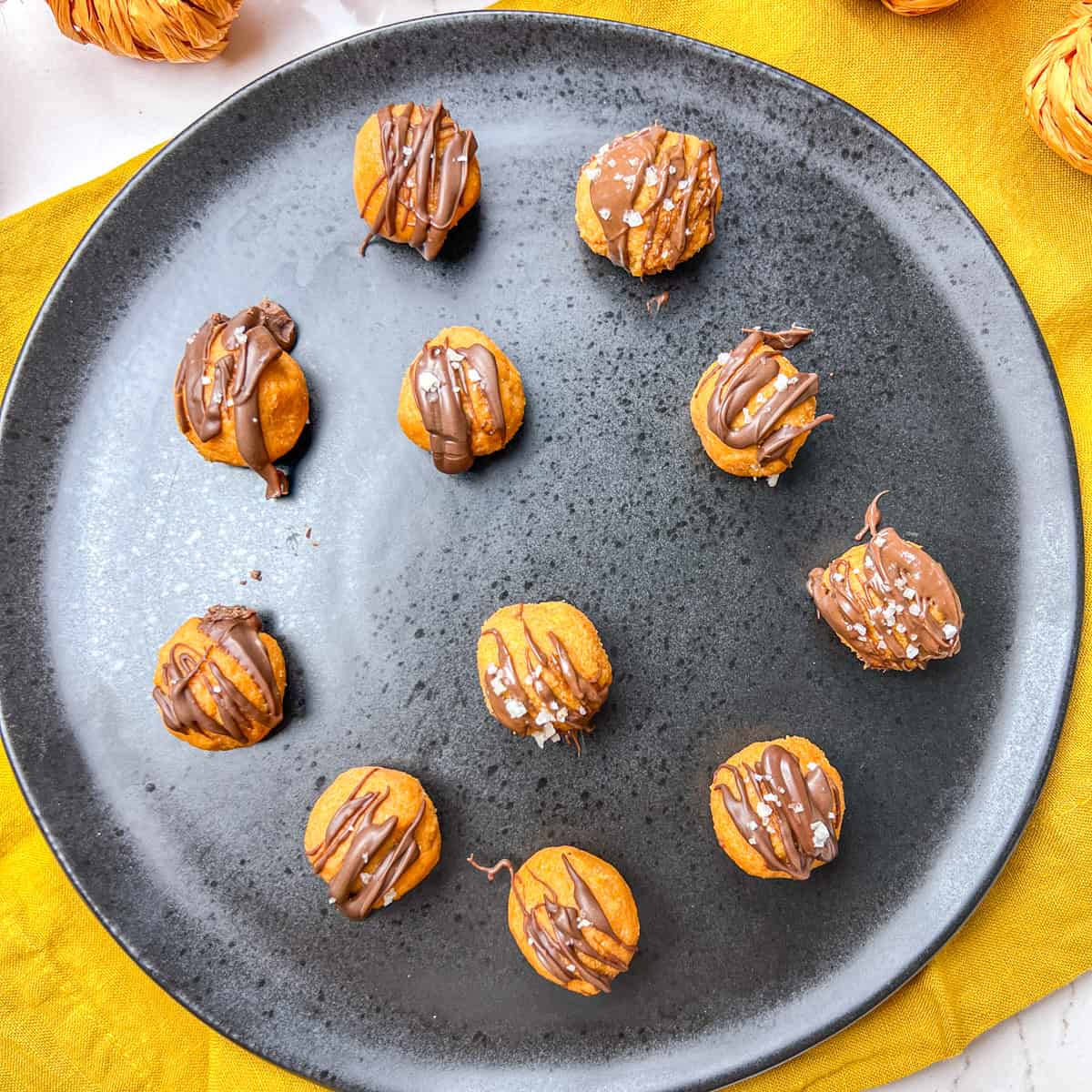 Pumpkin pie truffles on black plate with chocolate drizzled over top.