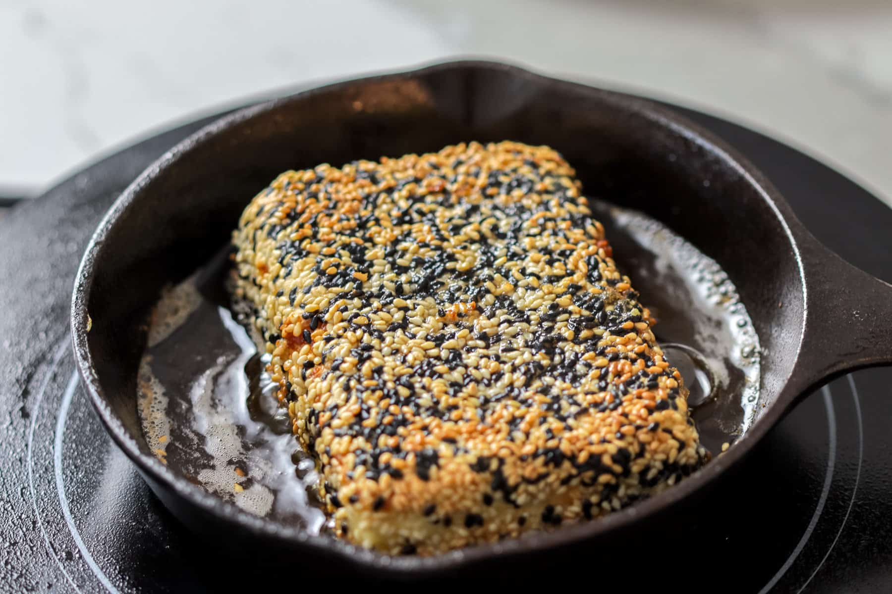 Fried feta cheese with sesame seeds in a cast iron skillet.