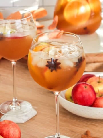 Apple cider sangria in a wine goblet with star anise and apples.