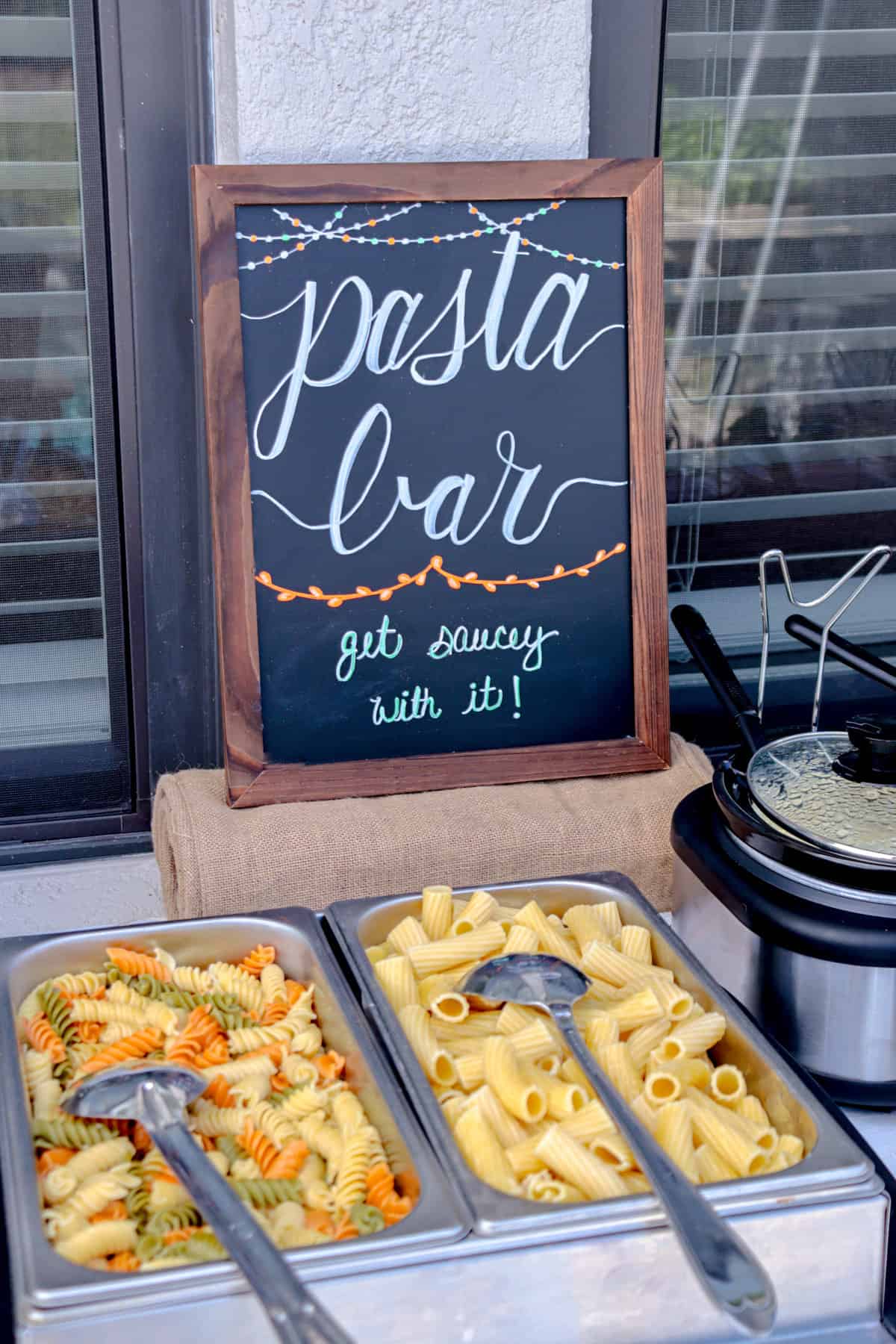 Pasta bar with pasta and chalkboard sign.