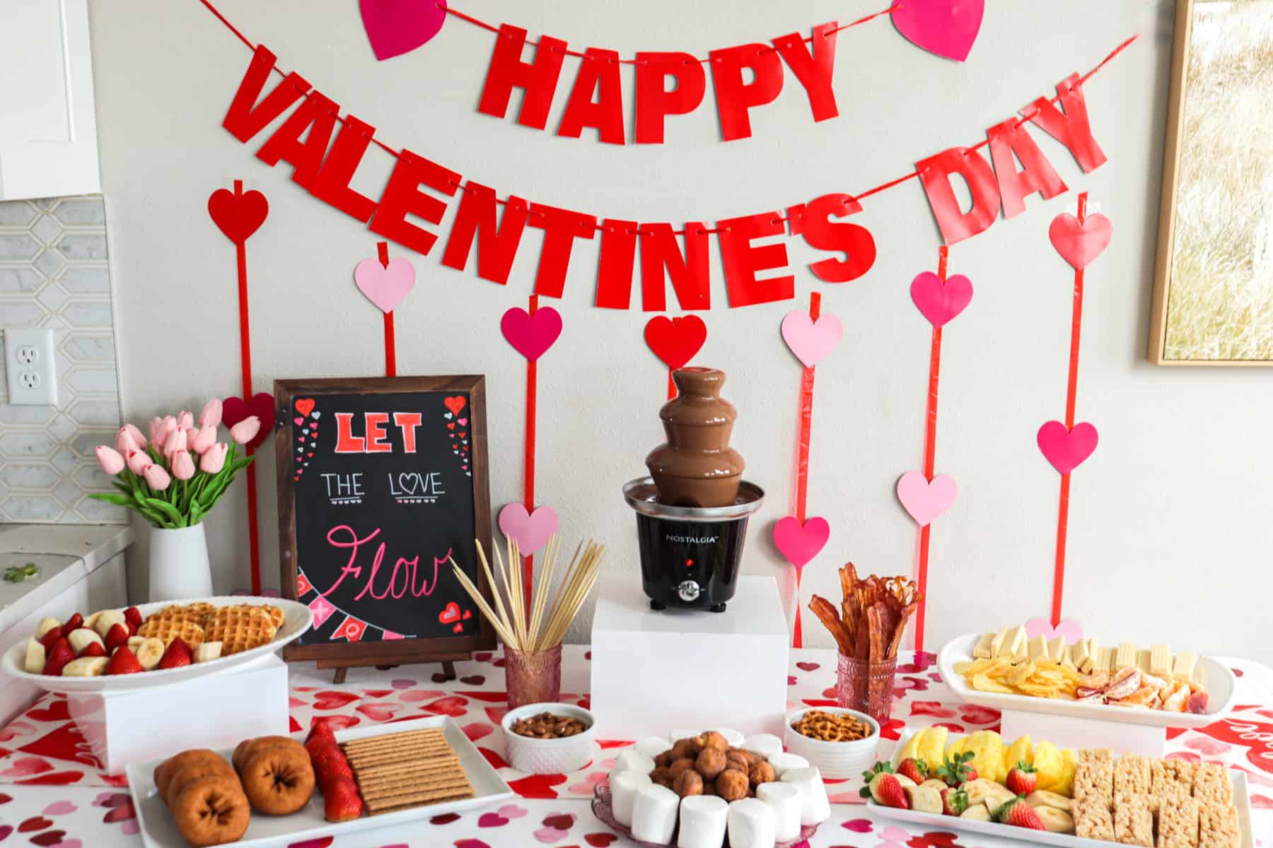 Valentine's Day chocolate fountain bar set up with a table full of dippers.