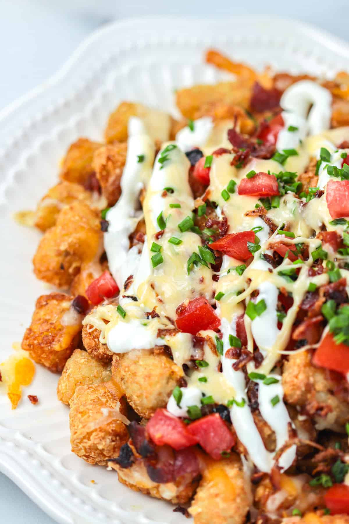 Tator tot nachos on a plate with cheese and sour cream.