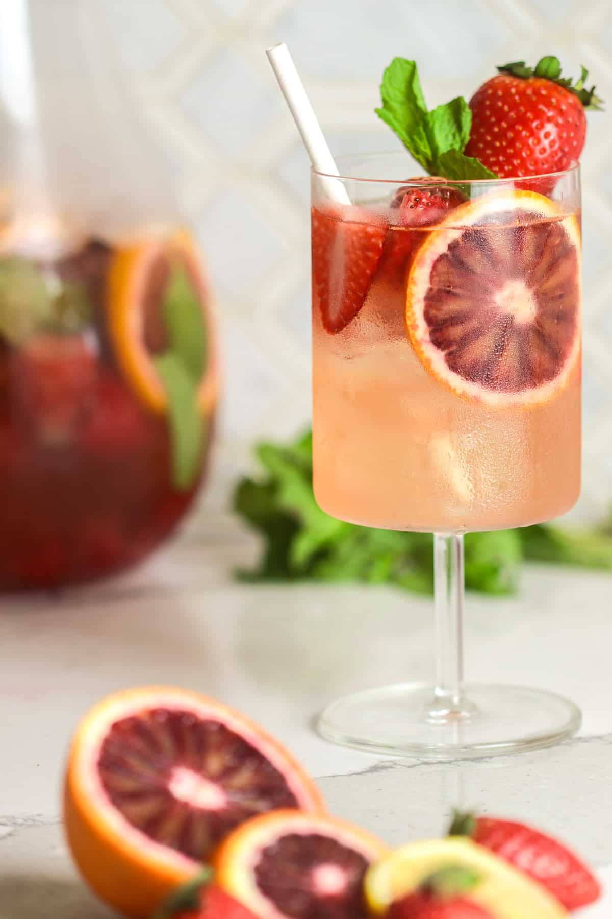 Glass of pink sangria garnished with strawberries and blood orange slices.