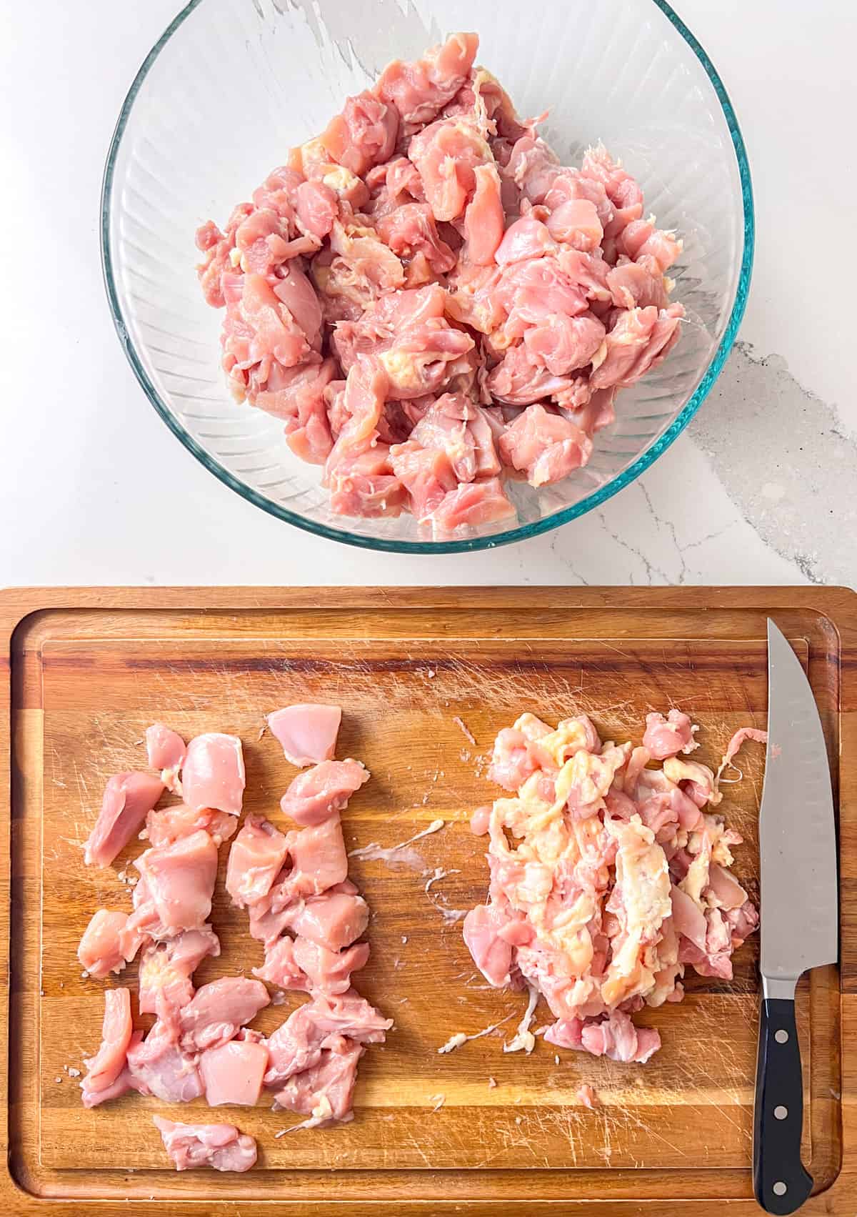 Raw chicken thighs being cut up with cubes.