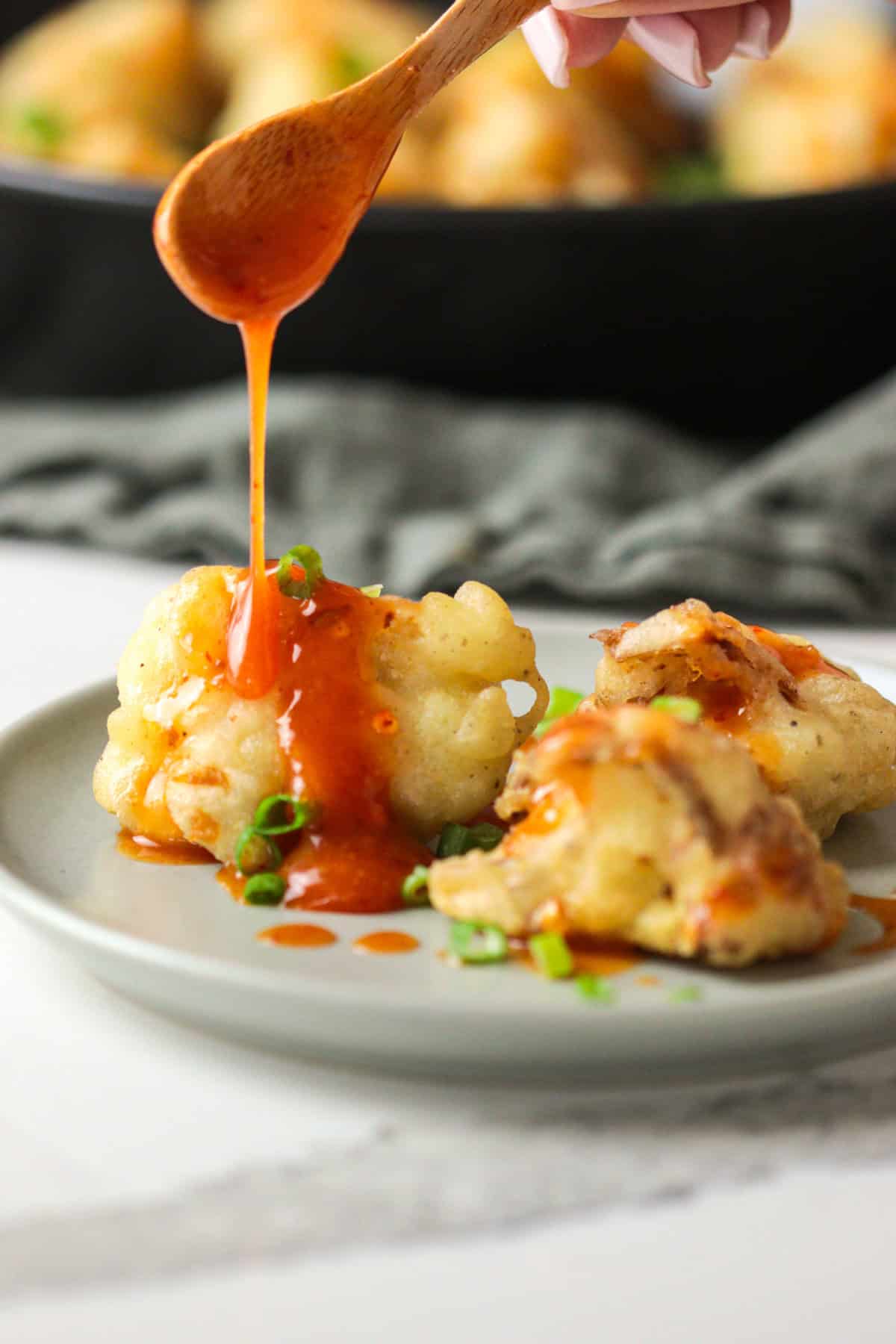 Spoon pouring sweet chili sauce over cauliflower.