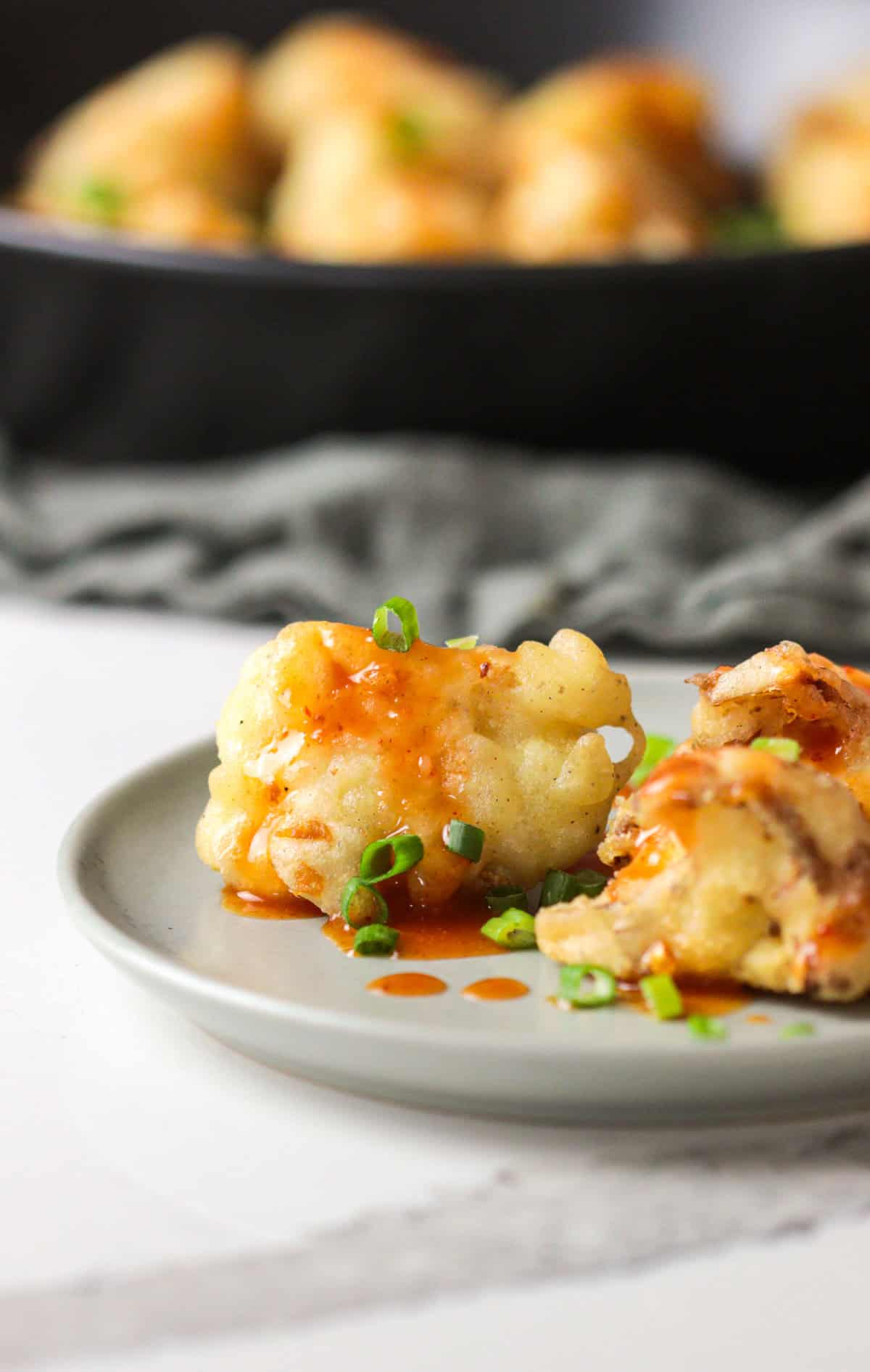 Fried cauliflower on a small plate with scallions and chili sauce.