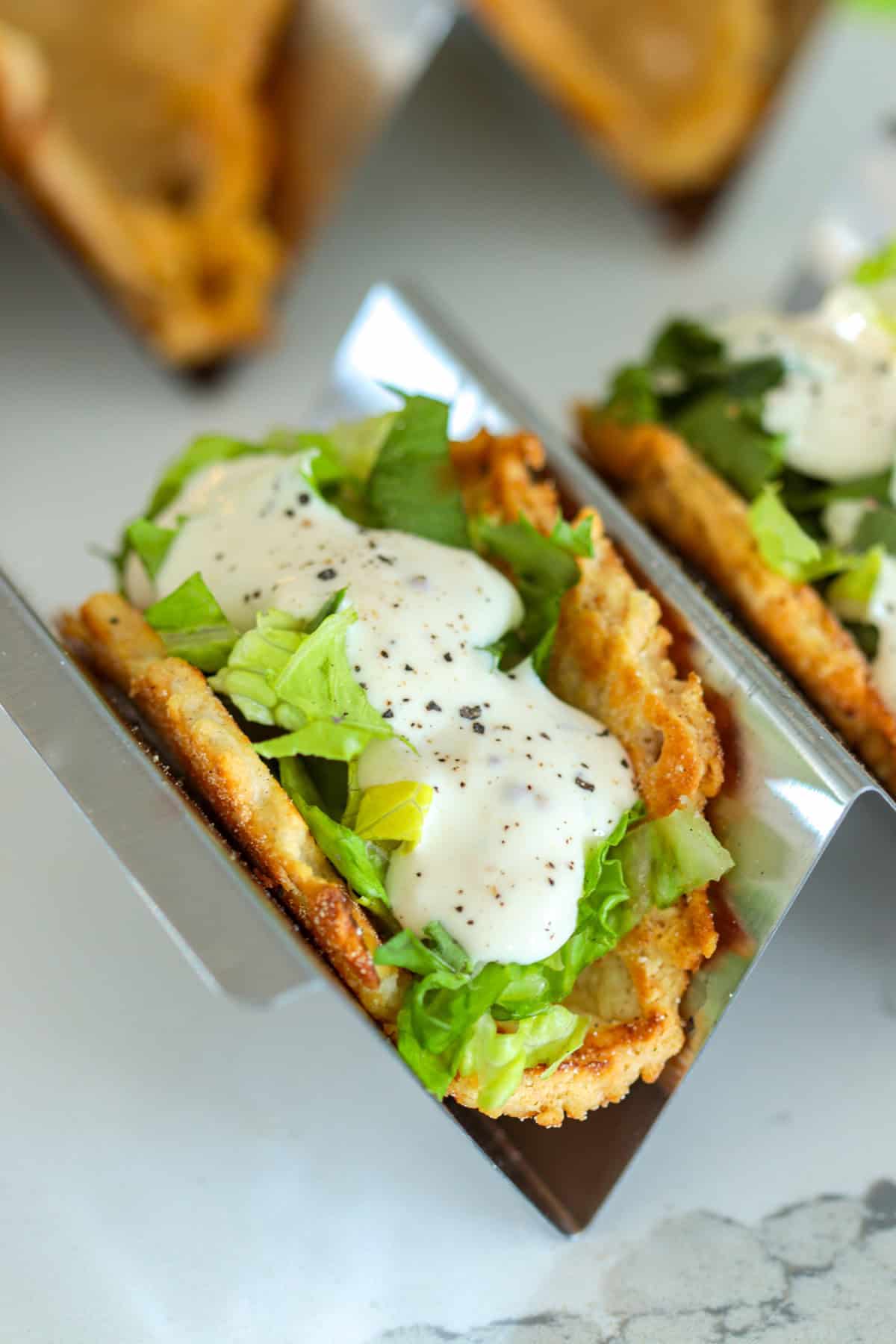 Caesar salad taco in a taco holder on table.