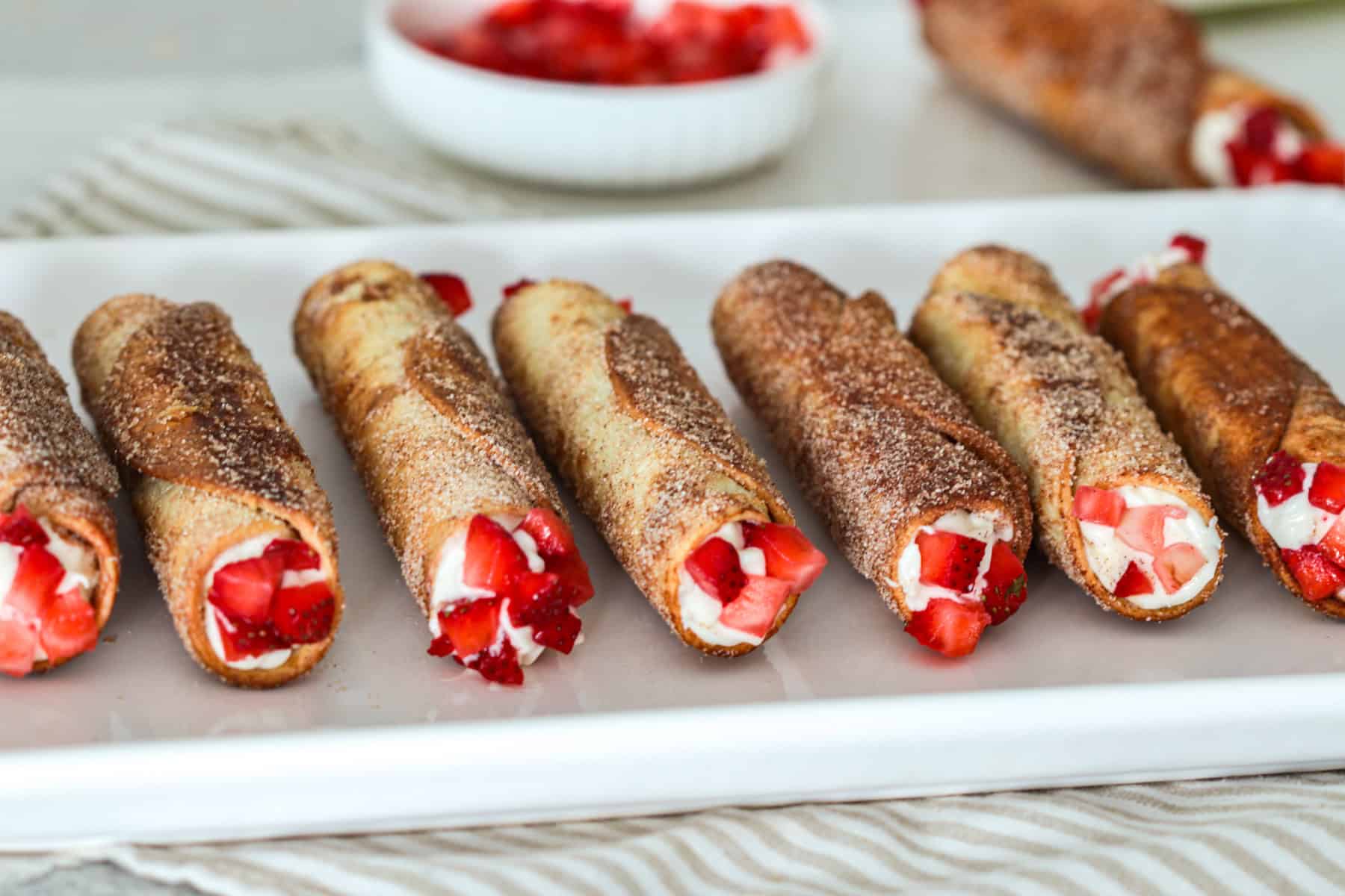 Cheesecake tubes on plate with strawberries.