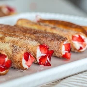 Cheesecake cigars on plate with strawberries.