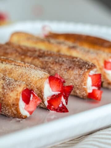 Cheesecake cigars on plate with strawberries.