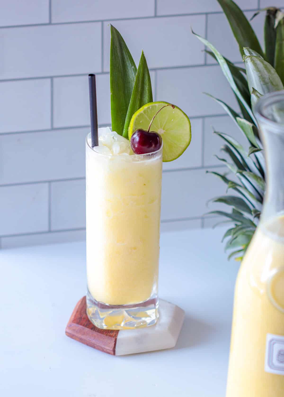 Blender free pina colada in a glass with a lime wheel, cherry and straw.