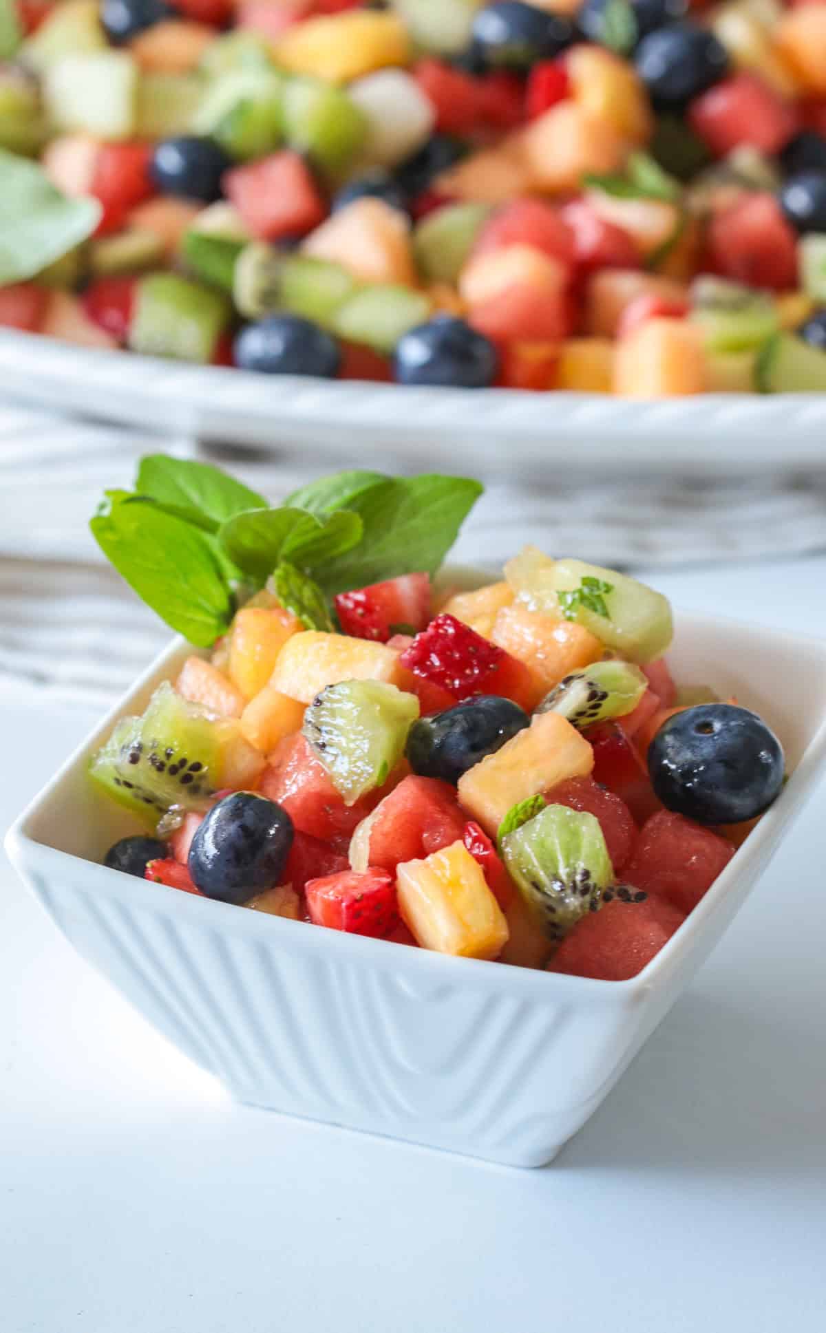 Chopped fruit salad in a white bowl with mint.