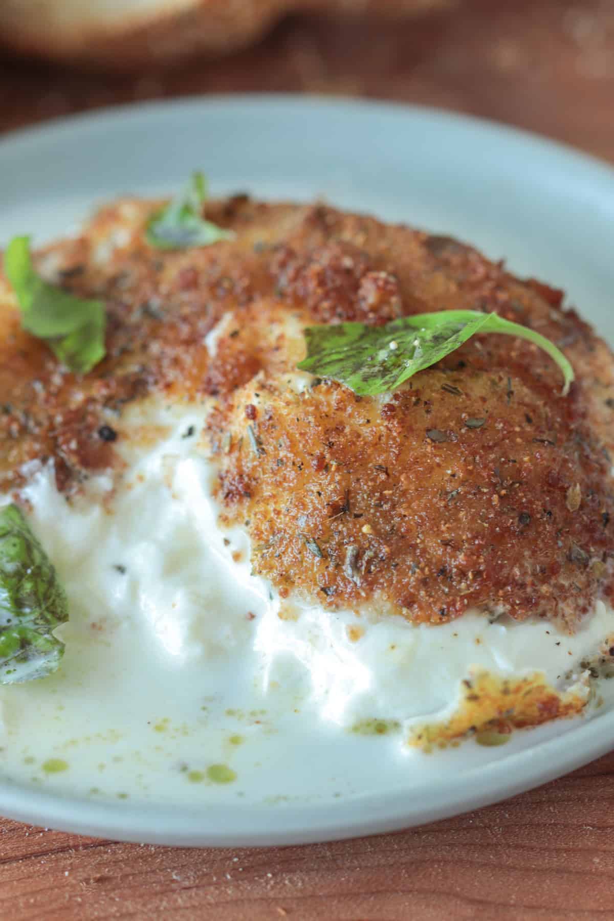 Fried burrata cheese on a plate with basil.