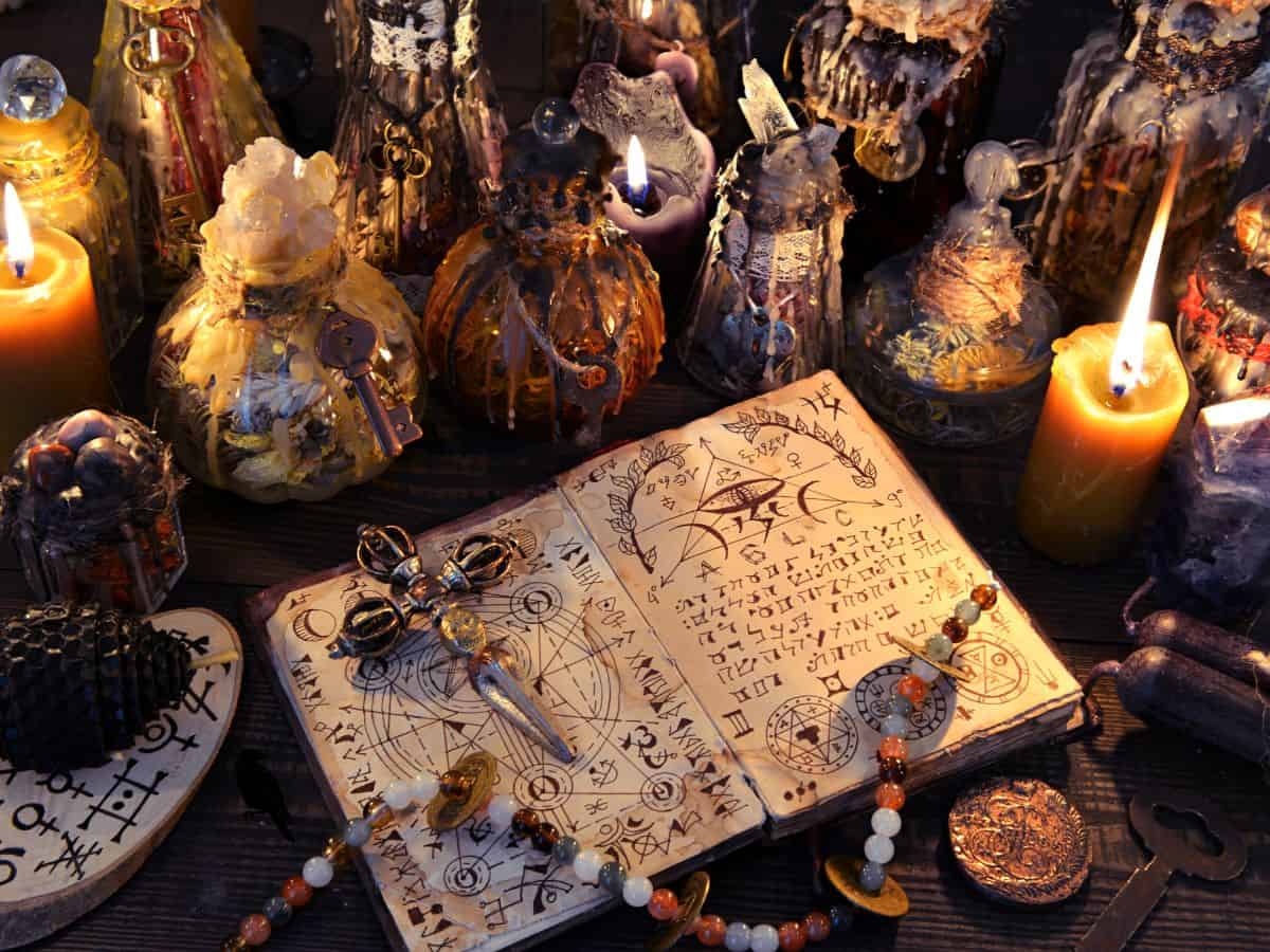 Lots of candles and a spooky witch spell book on table.