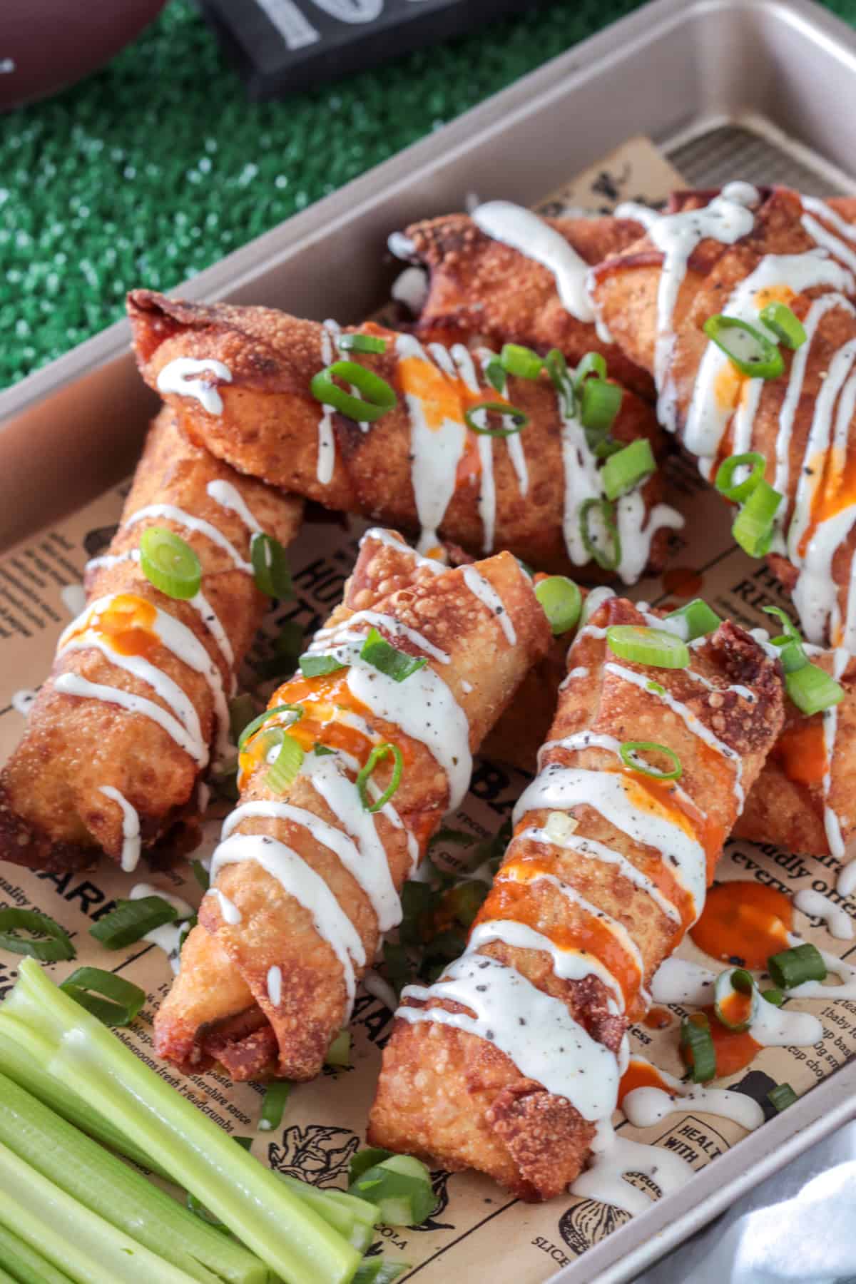 Buffalo chicken egg rolls on paper drizzled with ranch dressing.