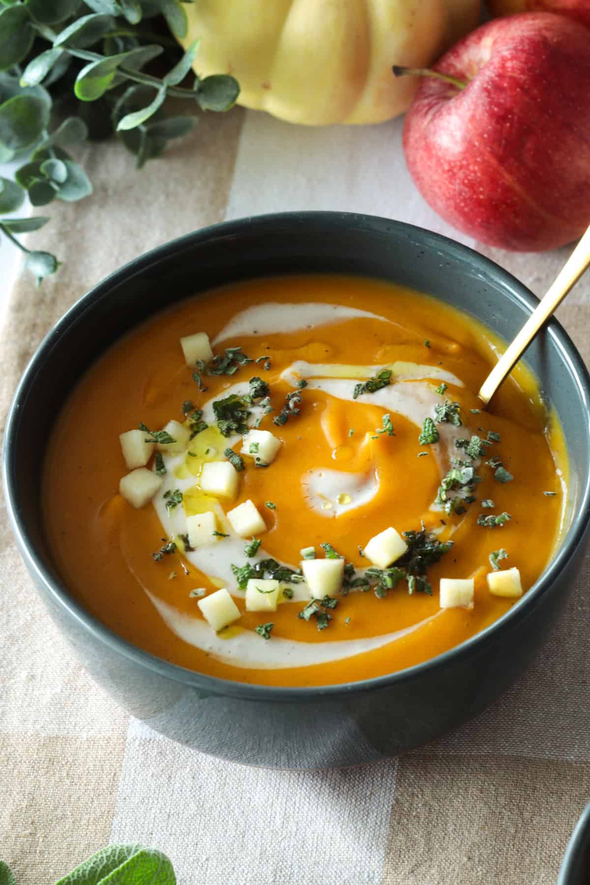 Butternut squash apple soup in a bowl with apples, sage and cream.