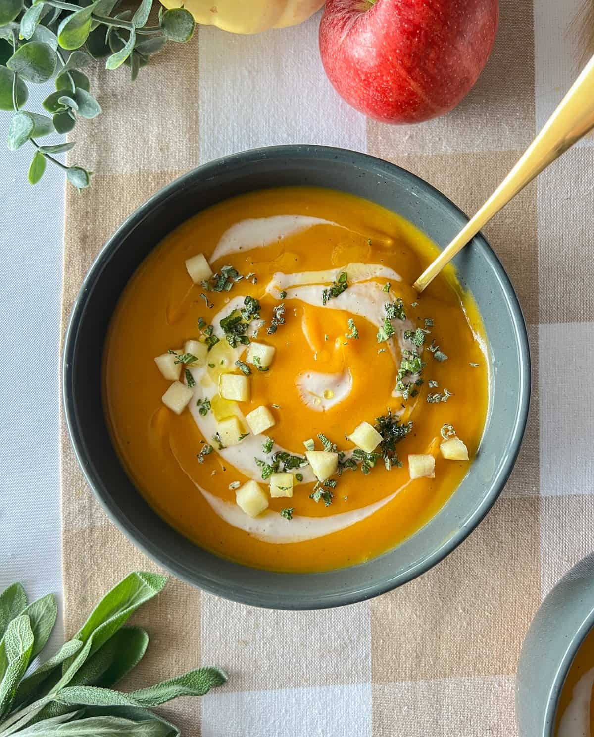 Butternut squash soup with apples, sage and cream in a gray bowl.