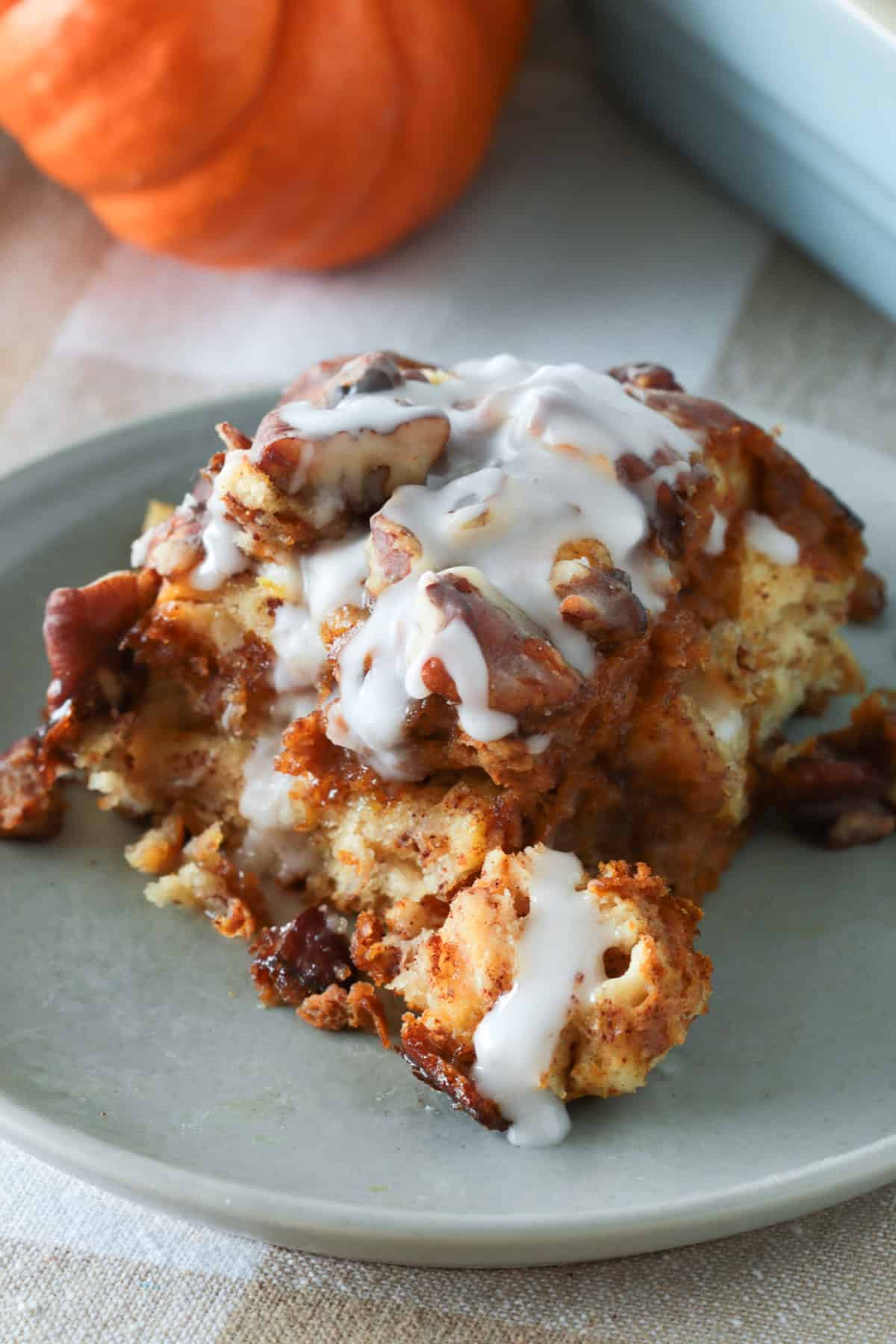 Pumpkin cinnamon roll french toast casserole on a plate with icing on top.