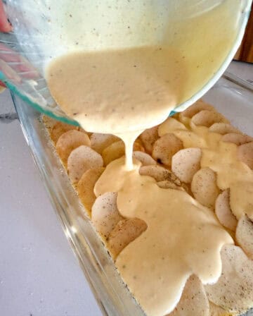 Pouring cheese sauce into sliced potatoes.