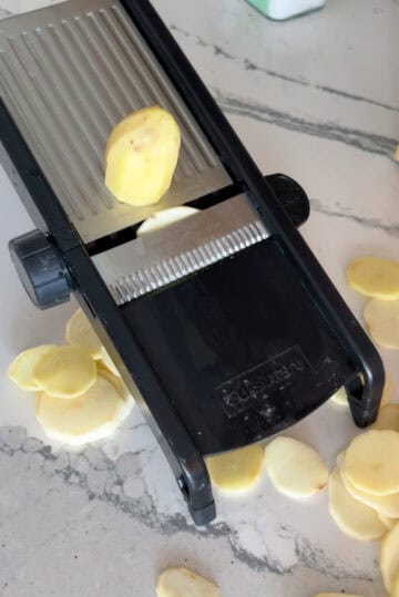 Cutting potatoes into thin slices using mandoline.