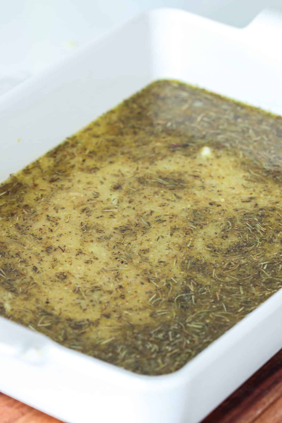 Greek potato seasoning with oil and broth in baking dish.