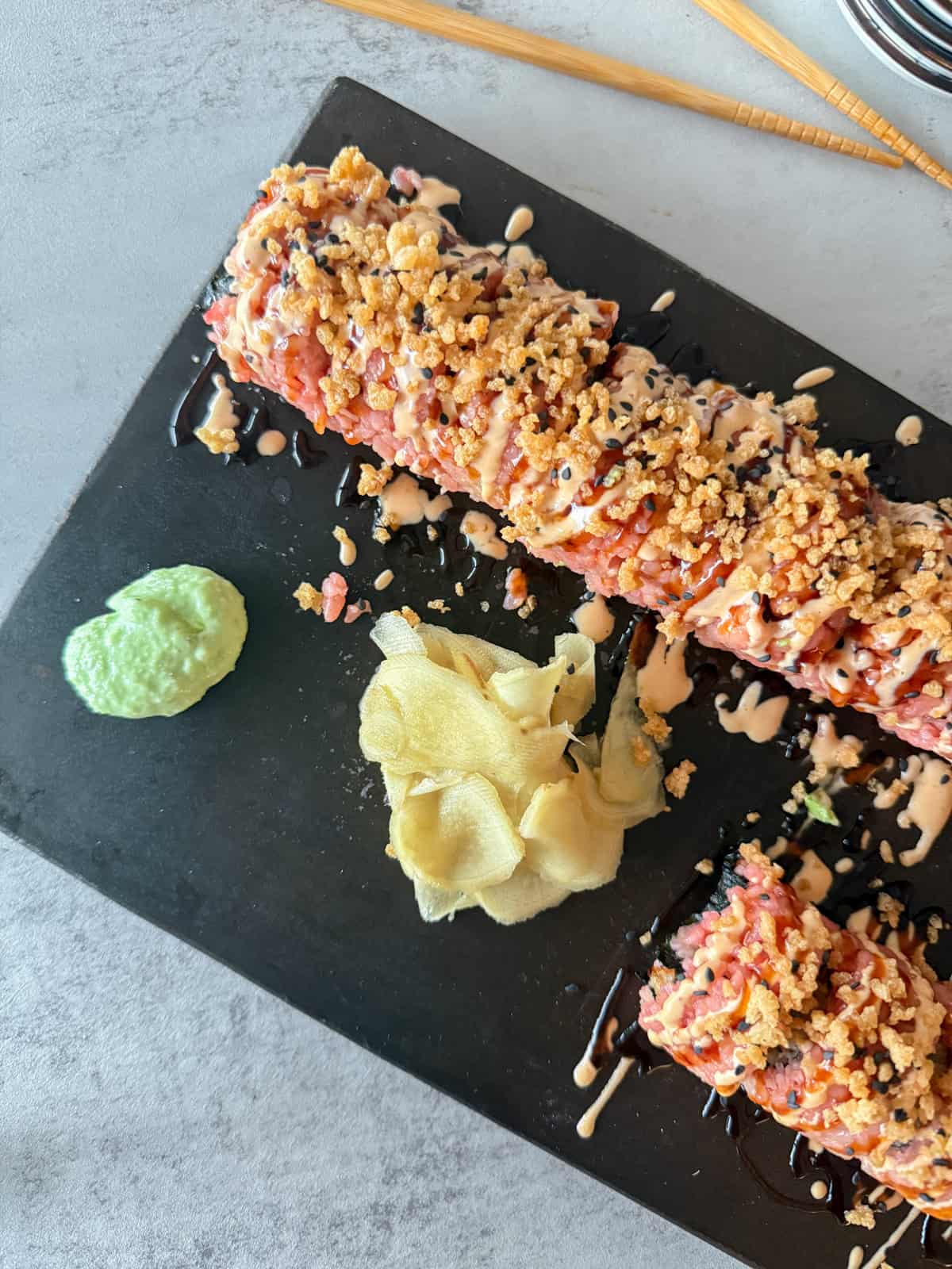 Pink sushi on cutting board with pickled ginger and wasabi paste.