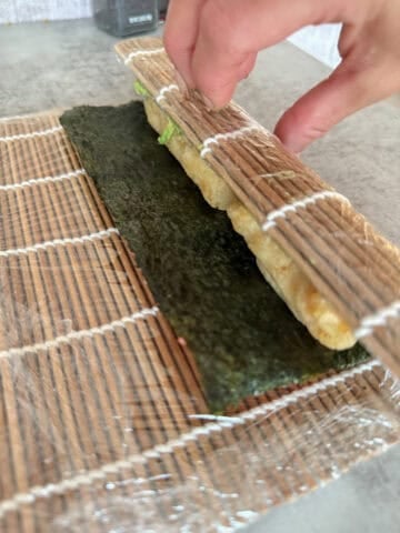 Rolling bamboo mat with nori, rice and sushi filling.