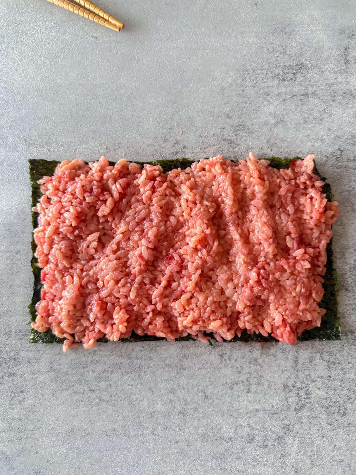 Pink sushi rice spread onto nori sheet.