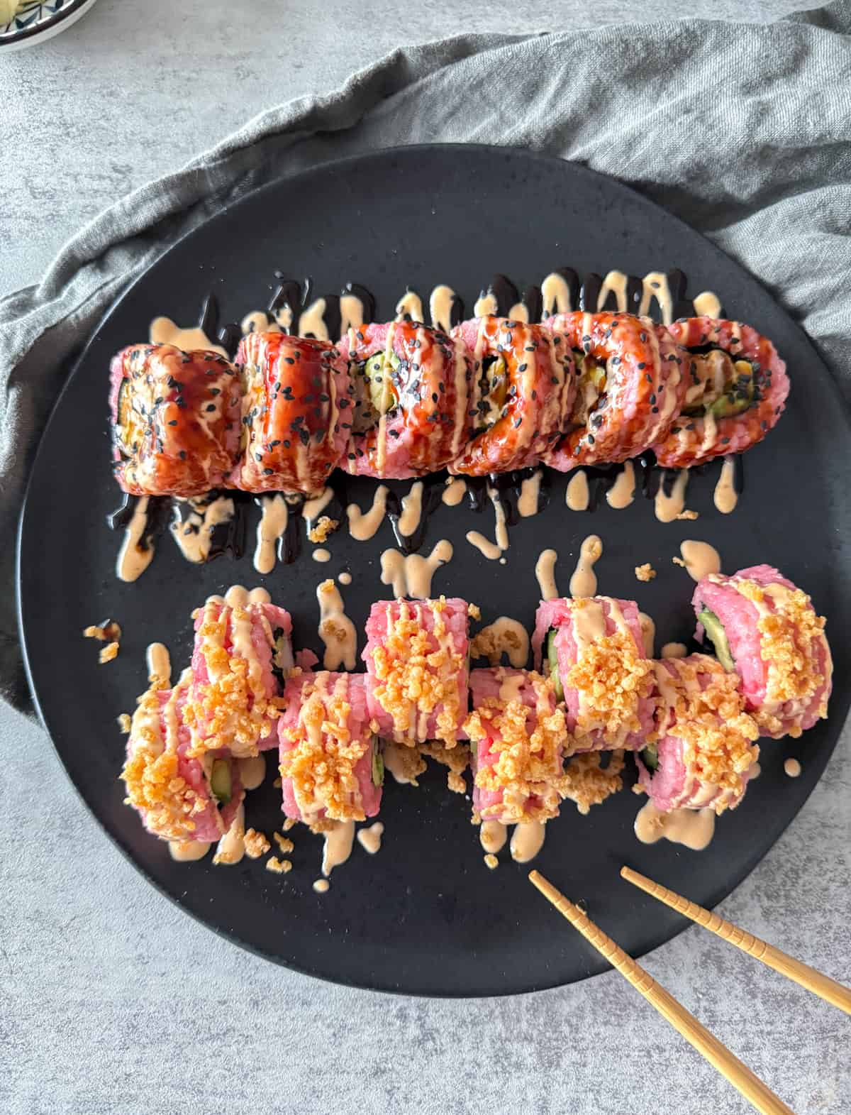 Pink sushi rolls on black plate with spicy mayo and crunch.