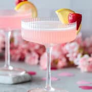 Pink cocktail with lemon strawberry garnish.