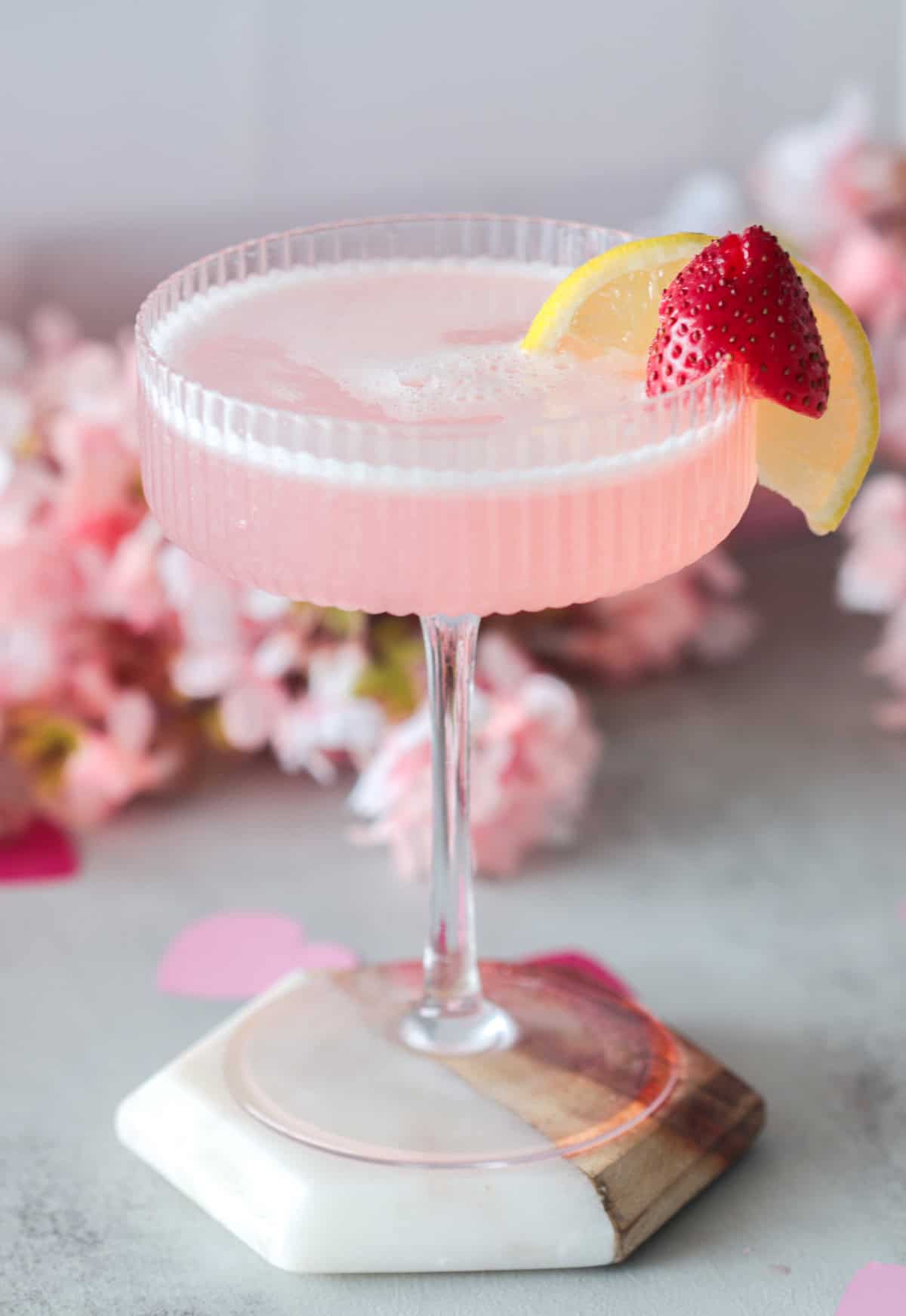 Pink cocktail with strawberry and lemon wedge.