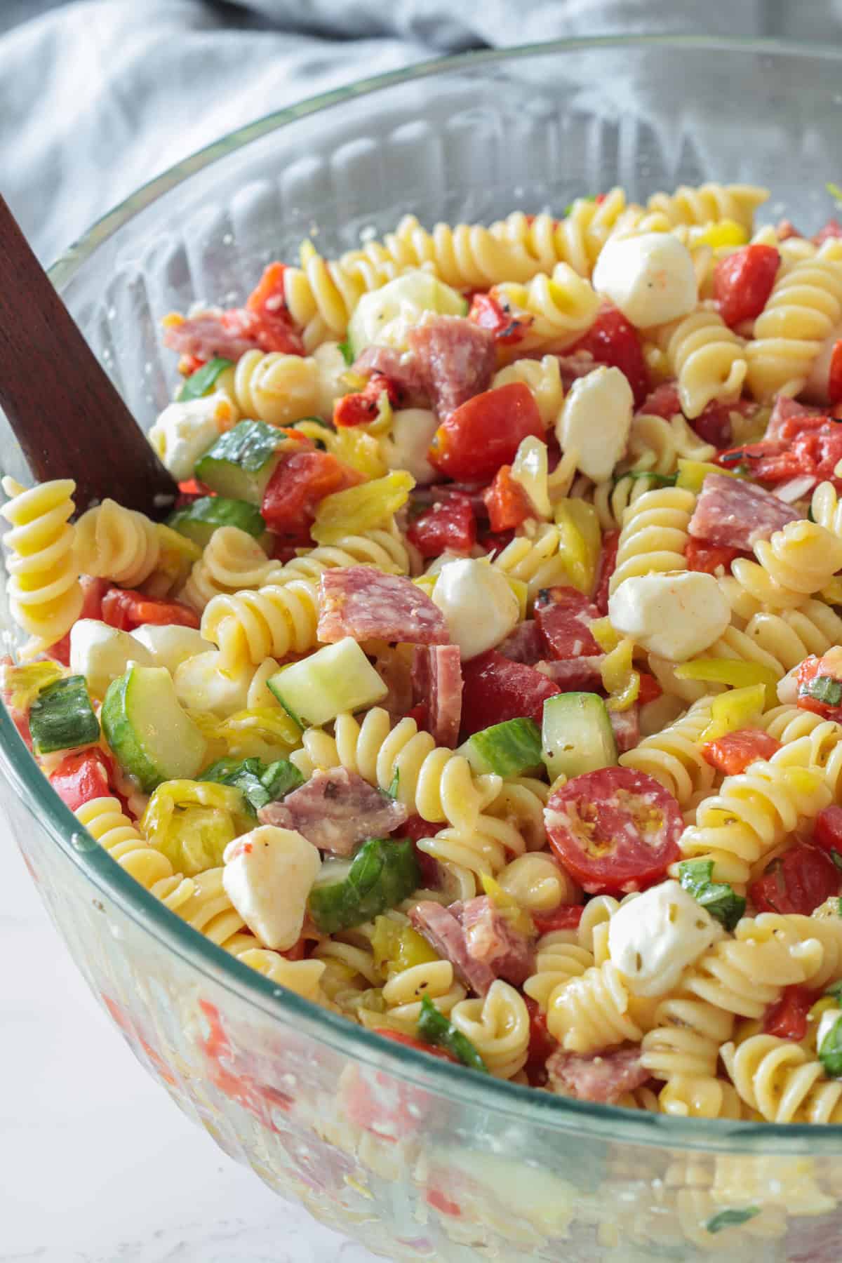 Italian pasta salad in a bowl with rotini, cucumbers, mozzarella, salami and peppers.