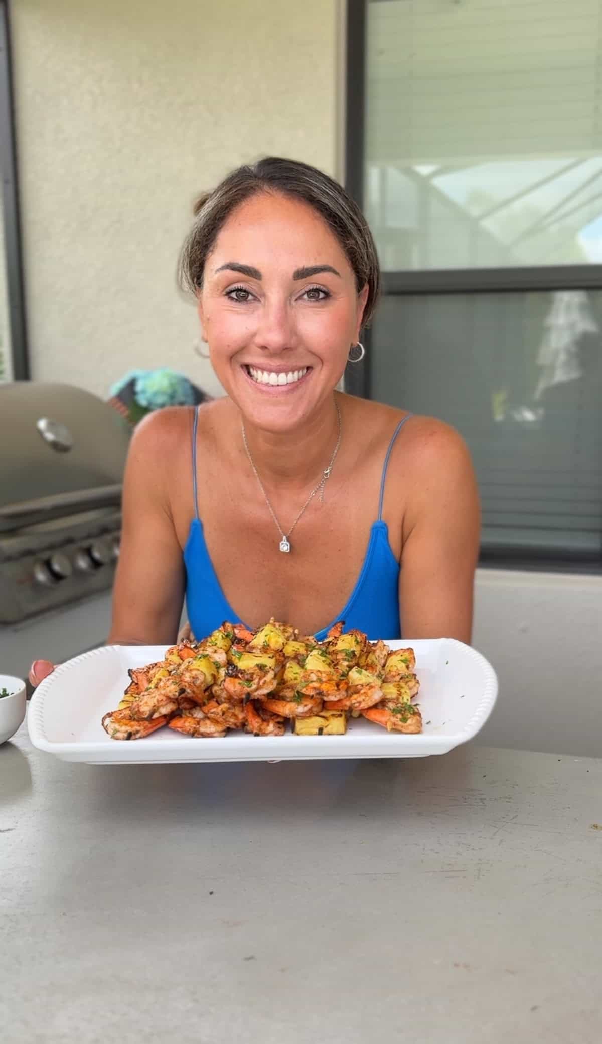 Aleka holding plate of pineapple shrimp skewers.