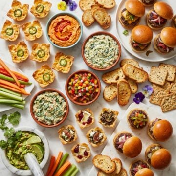 A colorful spread of easy party appetizers for a crowd including dips finger foods sliders and bite-size snacks on a marble surface