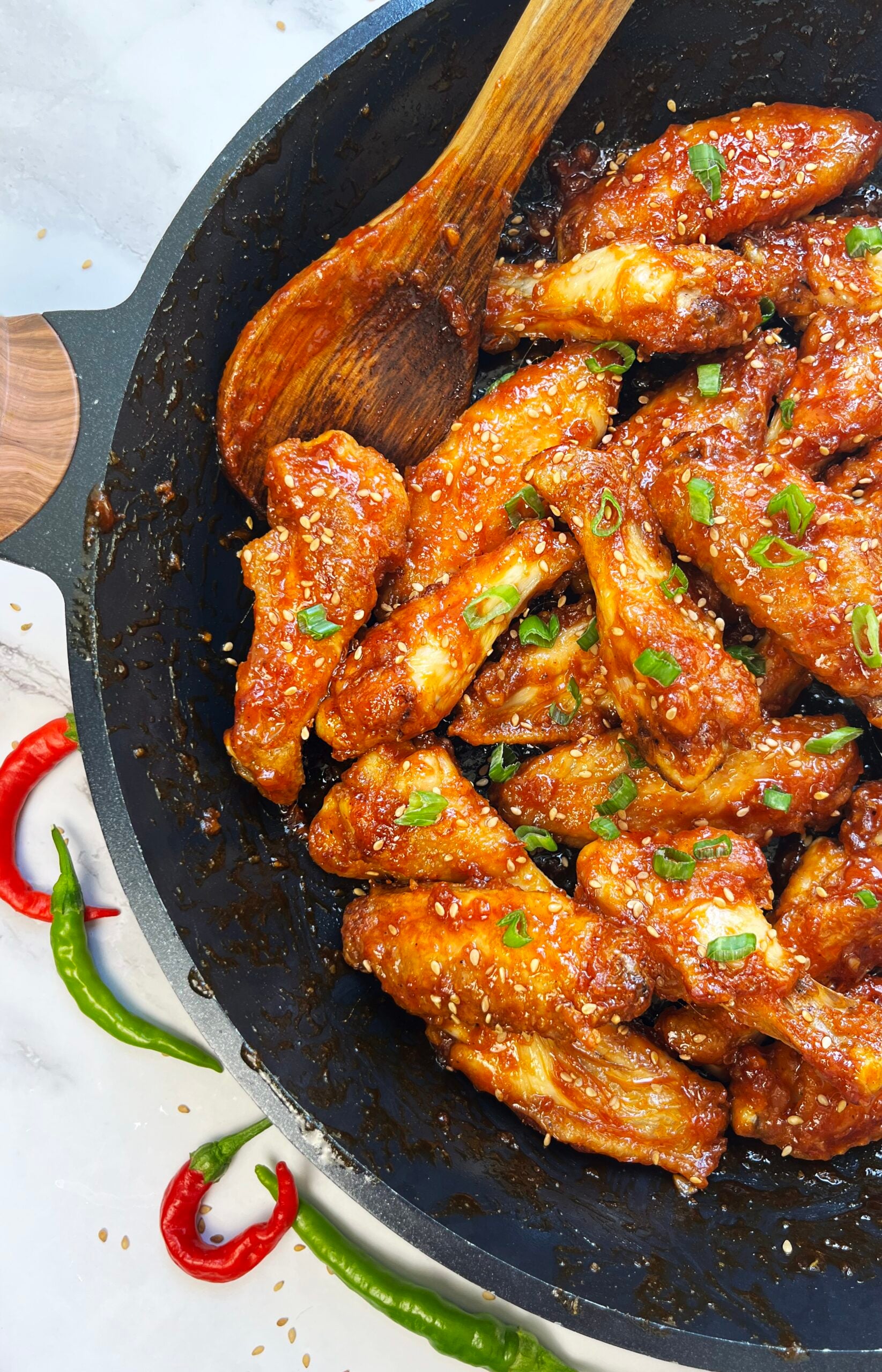 Sticky gochujang chicken wings in a skillet with sesame seeds and green onions.
