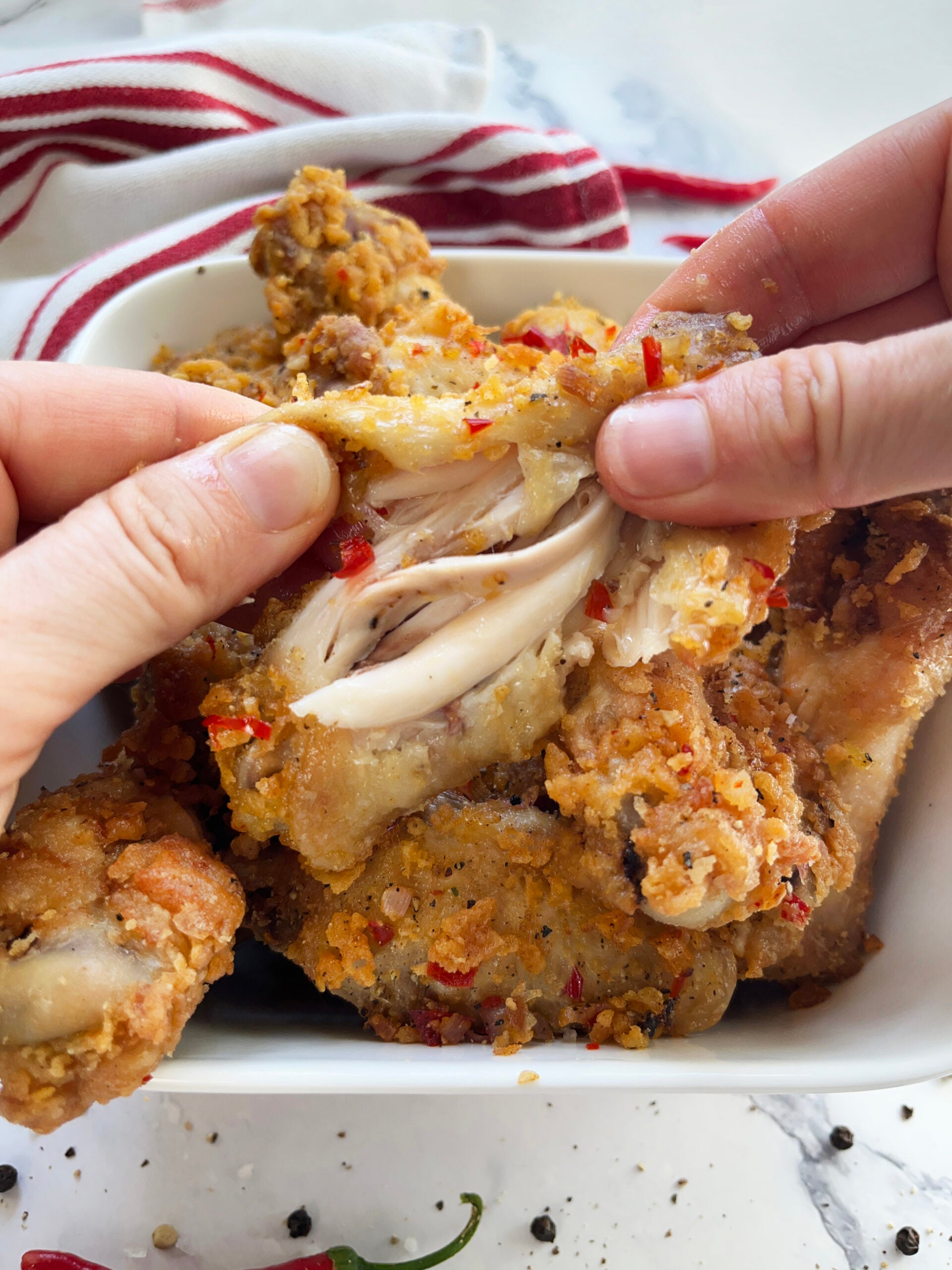 Crispy salt and pepper chicken wing pulled apart to show the juicy meat inside.