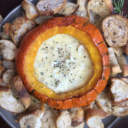 Baked pumpkin filled with melted Brie and herbs surrounded by toasted bread.