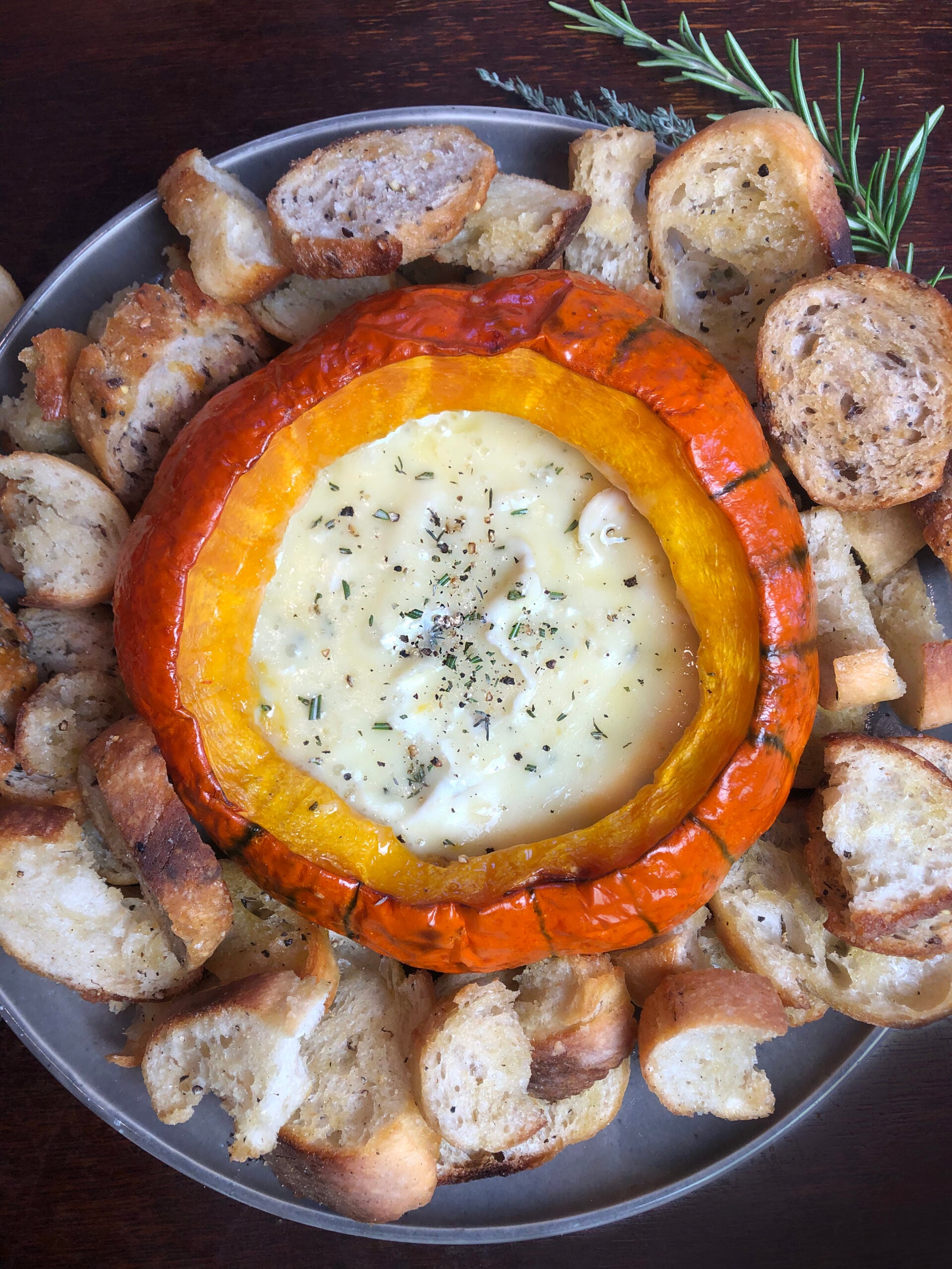 Baked pumpkin filled with melted Brie and herbs surrounded by toasted bread.