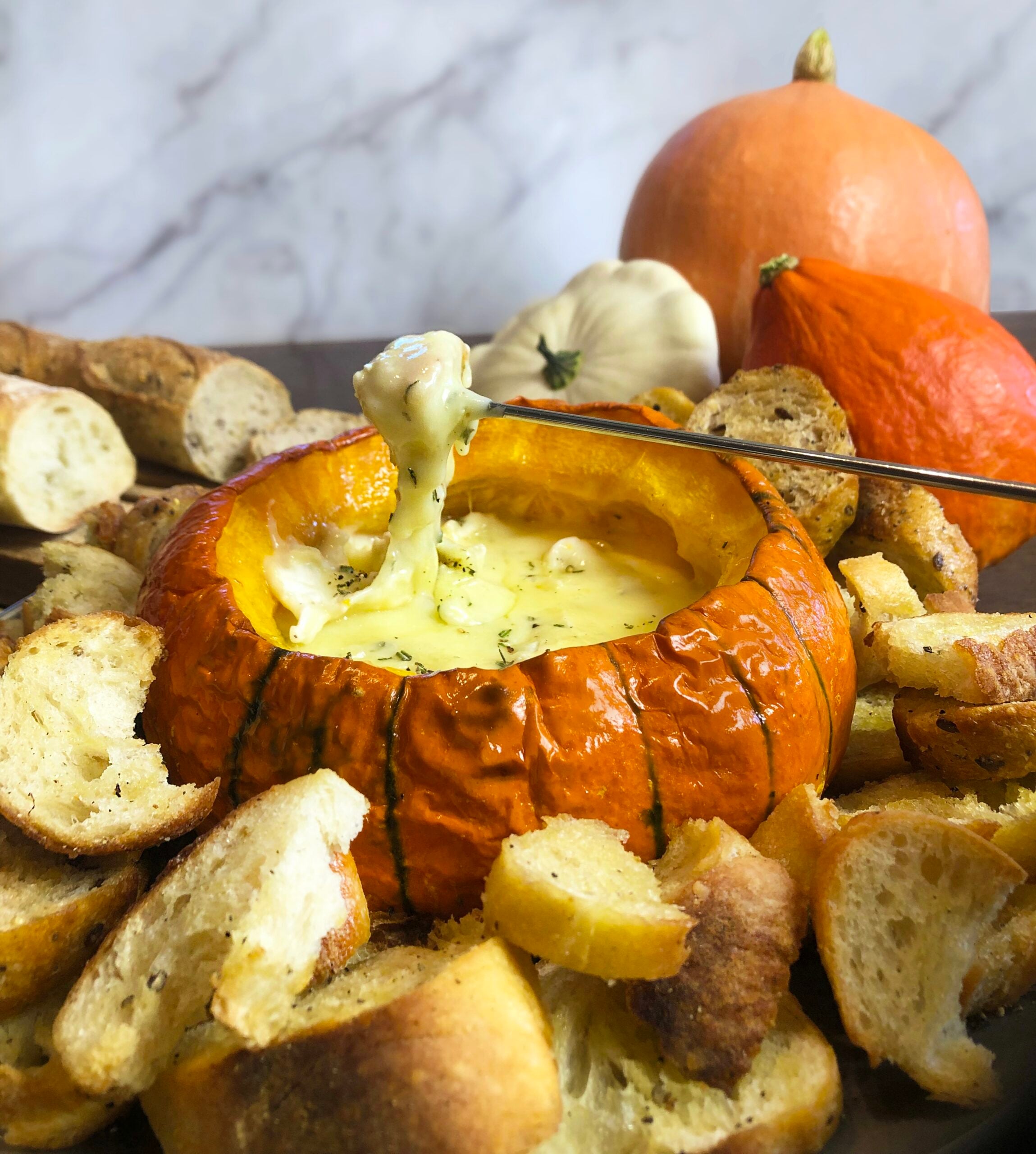 Melted Brie being lifted from a roasted pumpkin with a fondue fork.