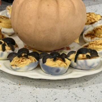 Spooky deviled eggs with olive spiders and spiderweb whites around a pumpkin