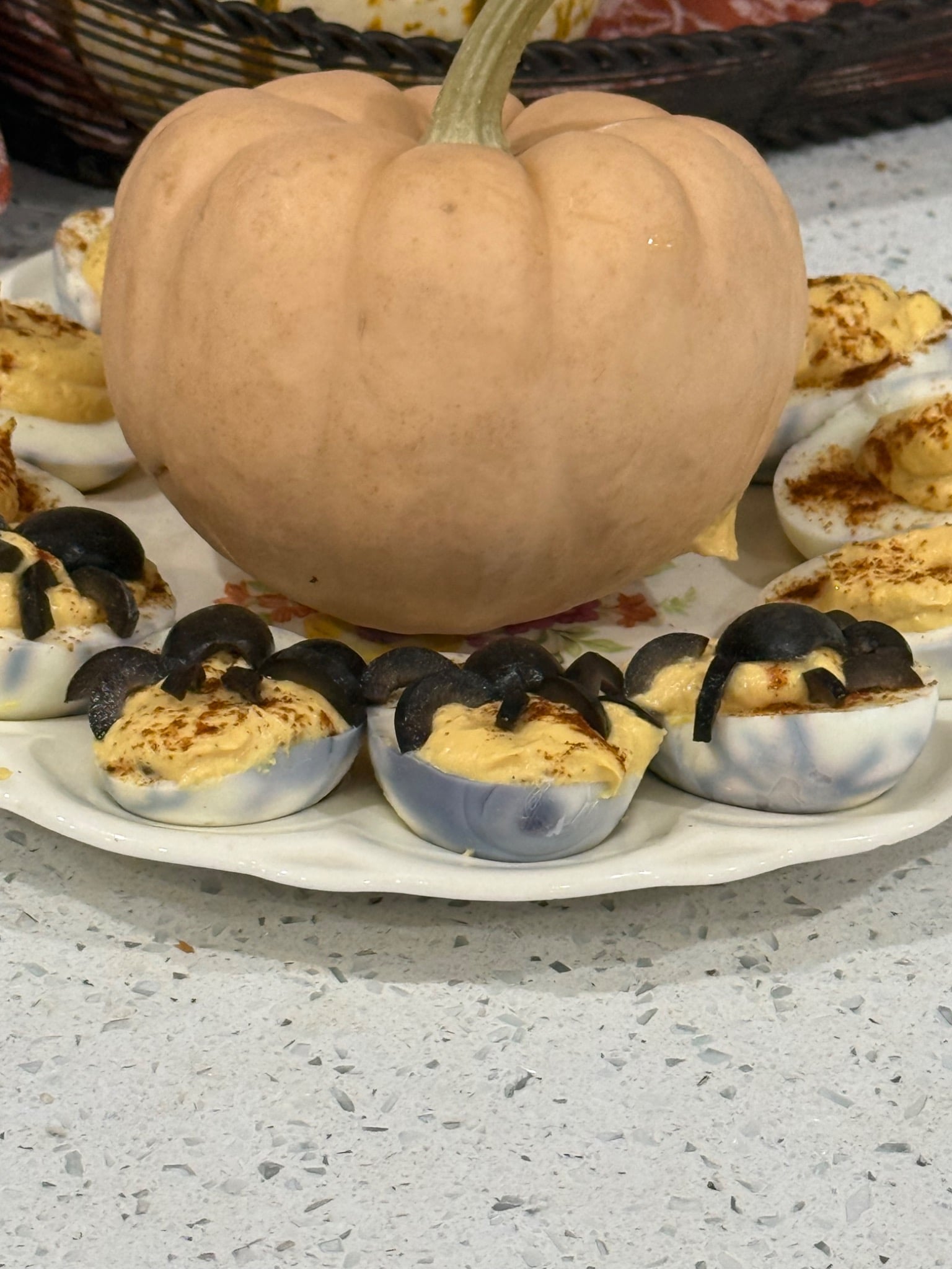Spooky deviled eggs with olive spiders and spiderweb whites around a pumpkin